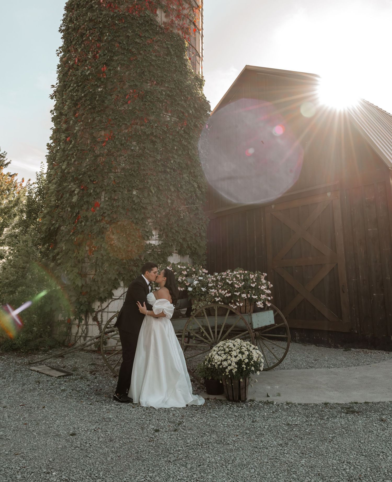 A romantic wedding portrait at sunset with an ivy-covered barn and rustic floral decor.