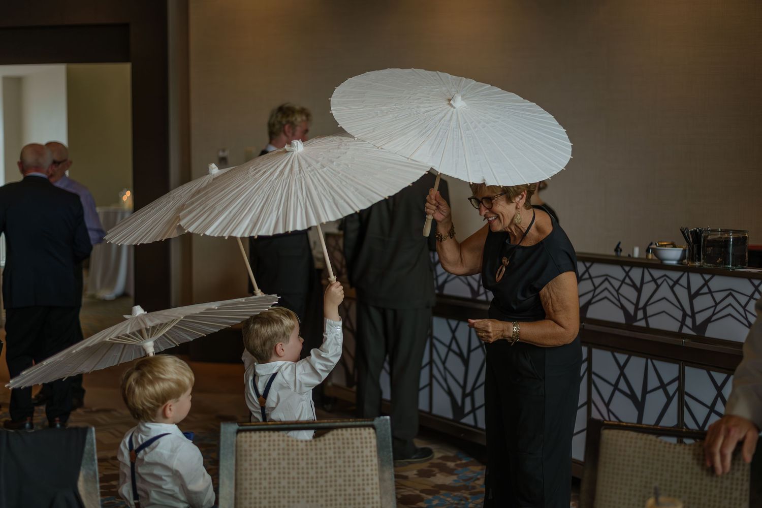 Wedding guests mingle under white parasols during an indoor reception event.