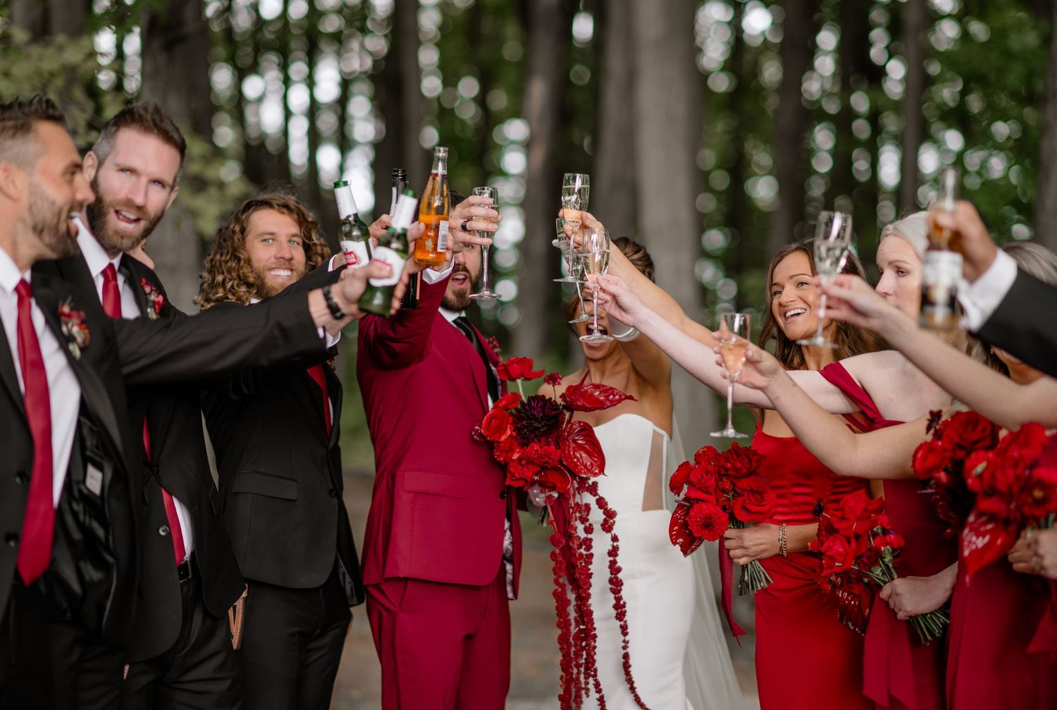 Wedding party in burgundy and white attire celebrating joyfully outdoors.