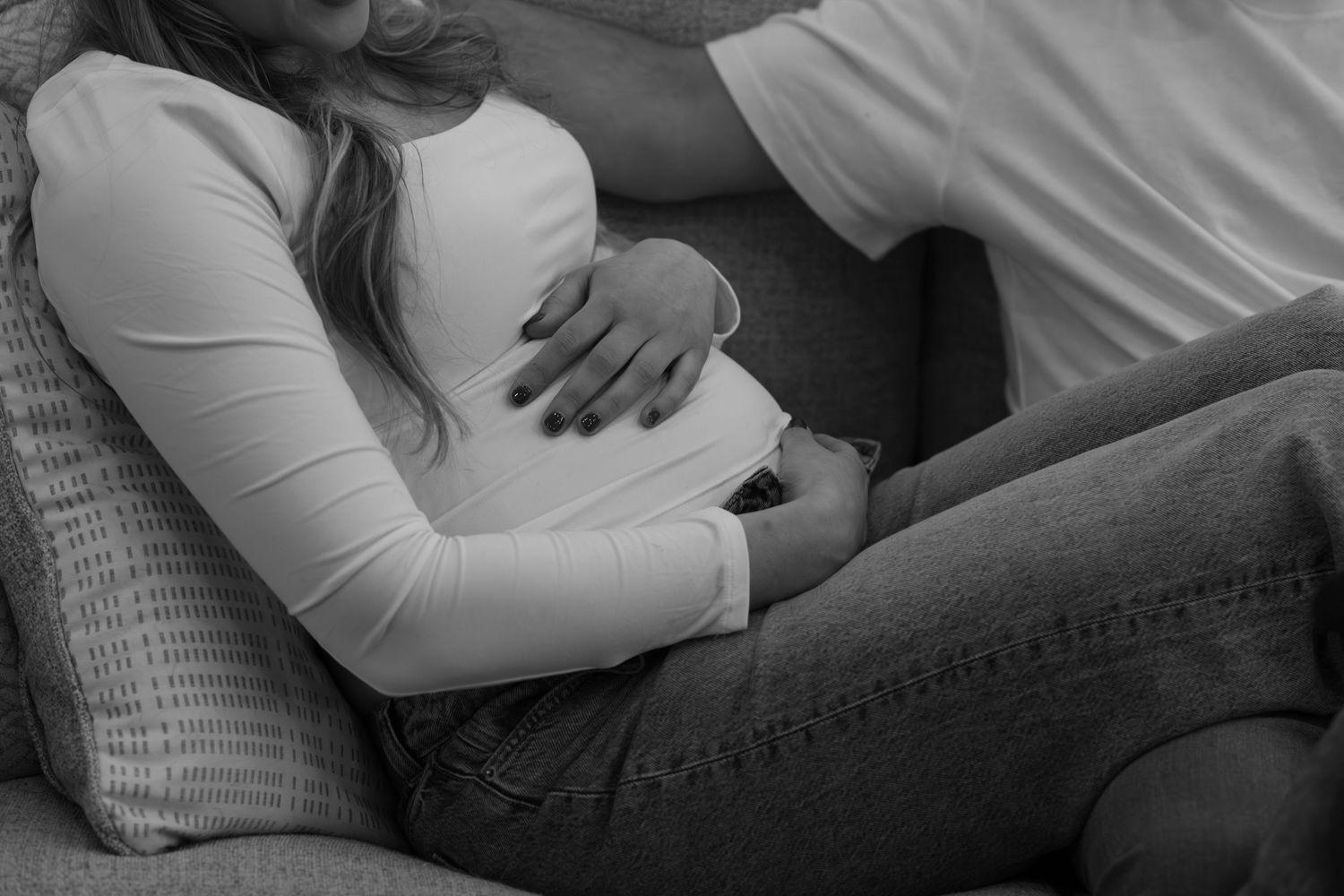 Cozy maternity photos of couple lounging together on grey cushions.