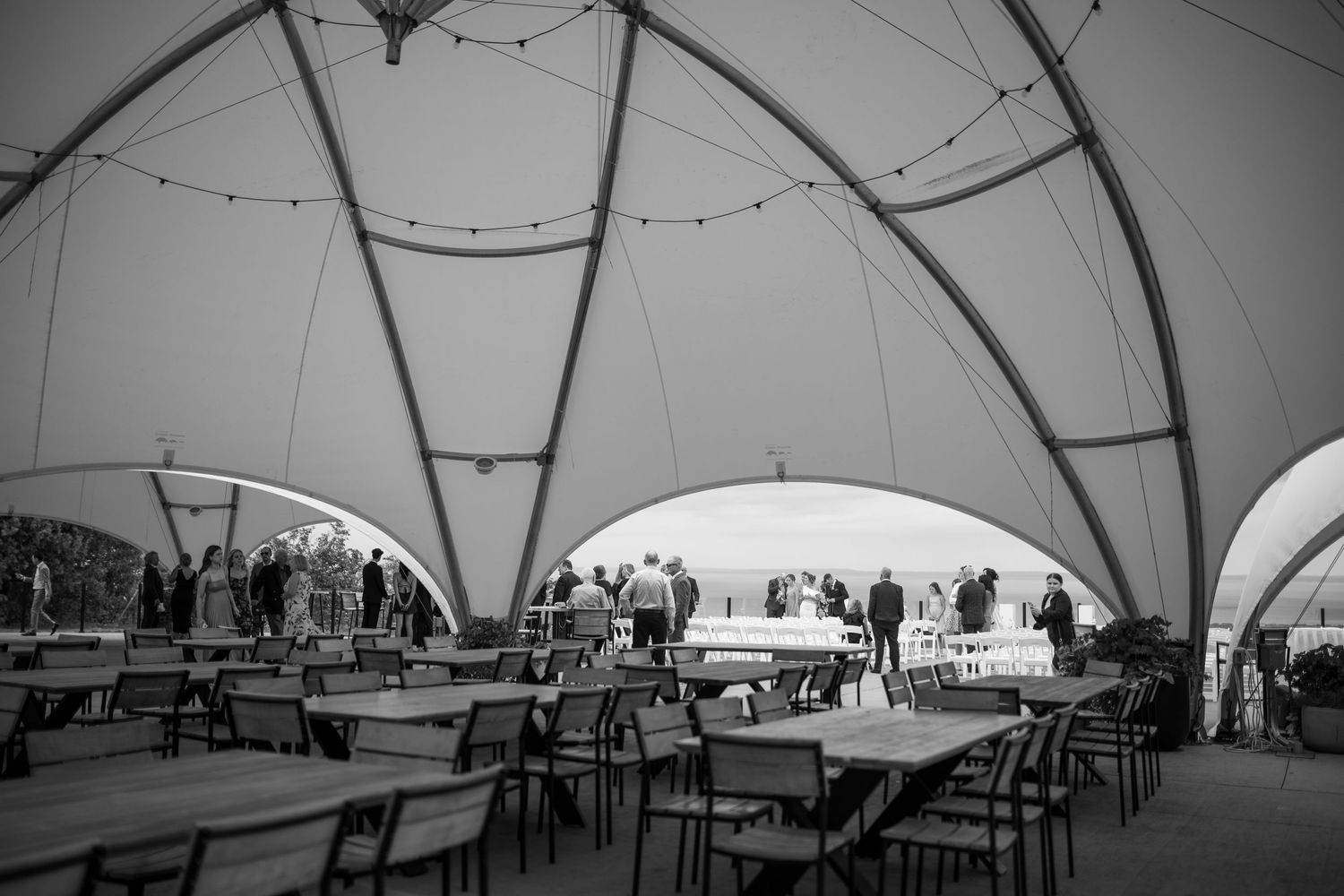 String lights hang inside a large white tent structure with tables and chairs set up for an event.