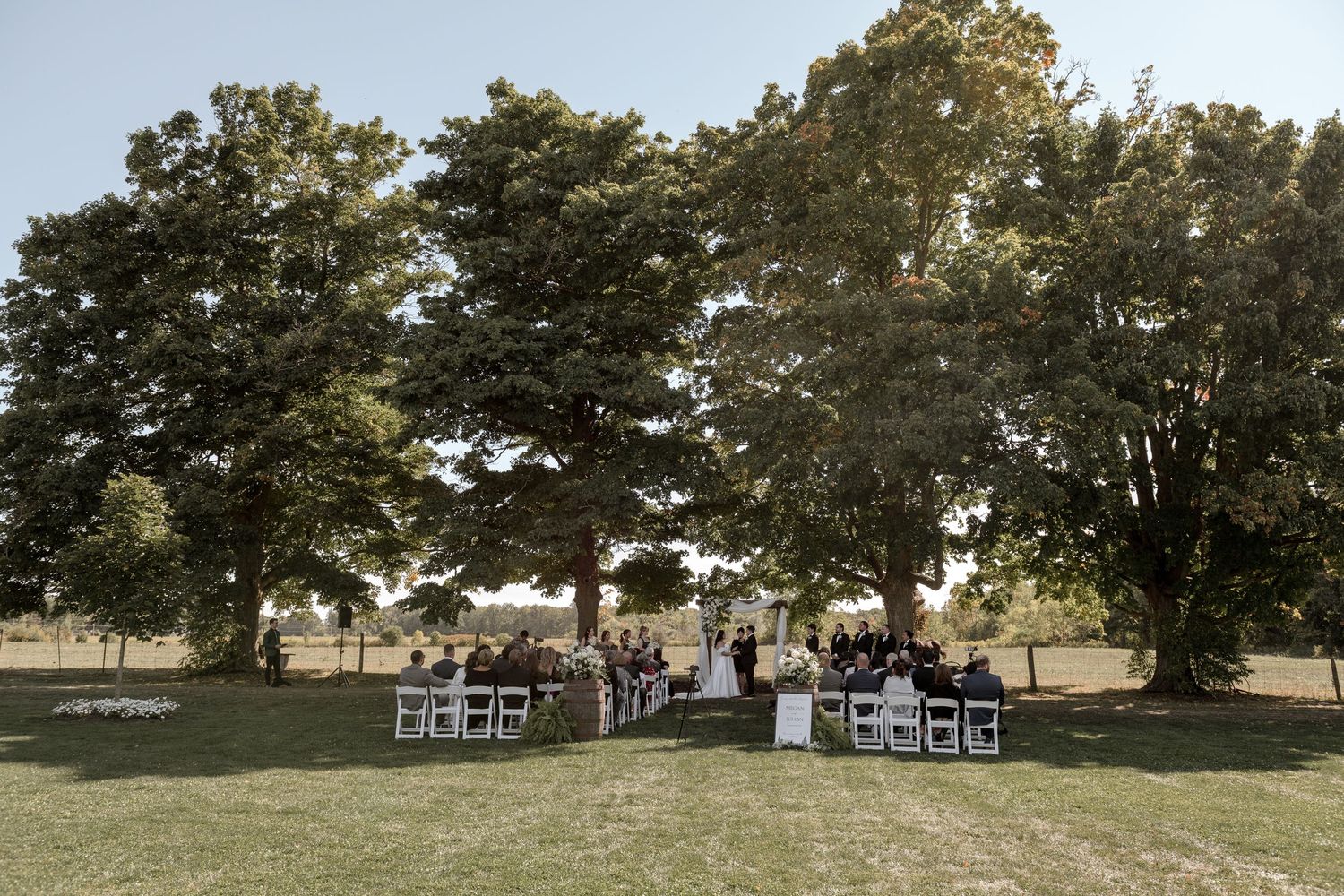 A panoramic view of a grassy field with scattered trees and a white house visible in the distance.