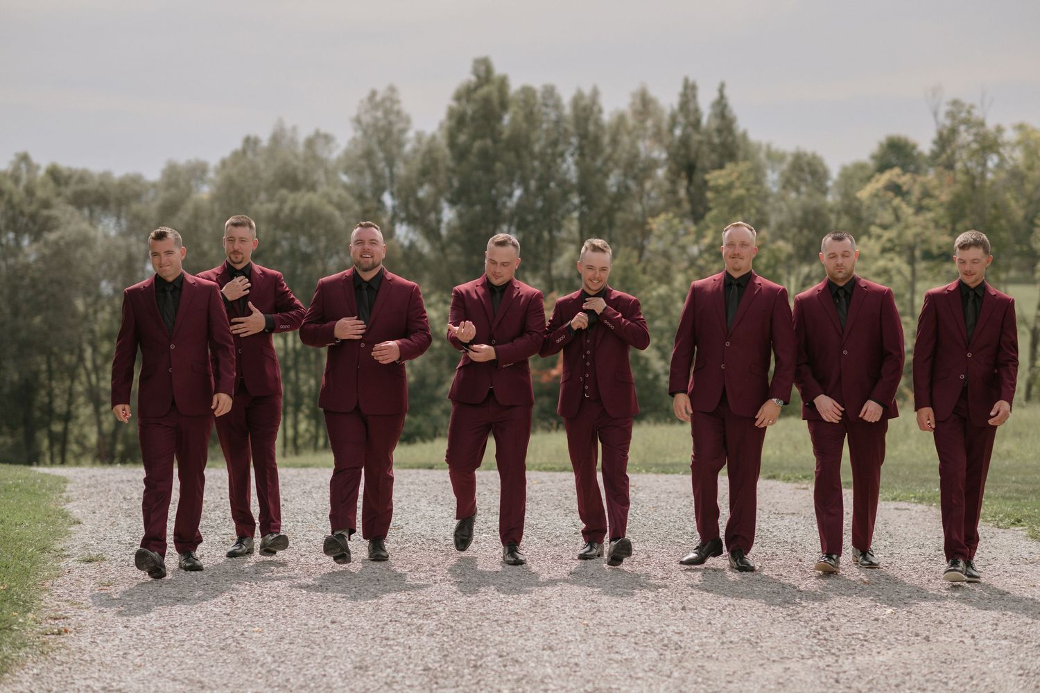 Groomsmen in burgundy suits posing together outdoors.