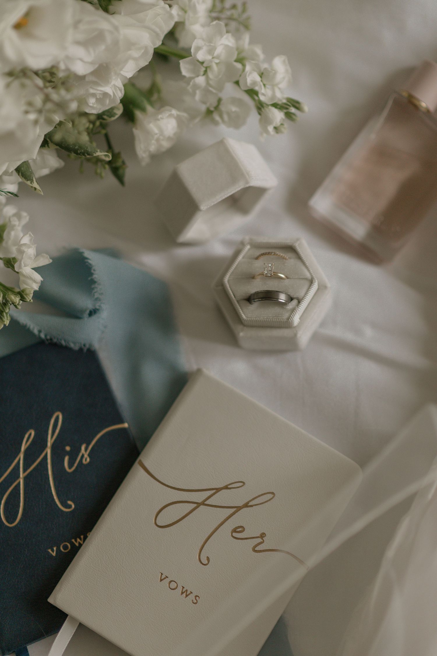Wedding vow books and rings displayed with white floral decorations.