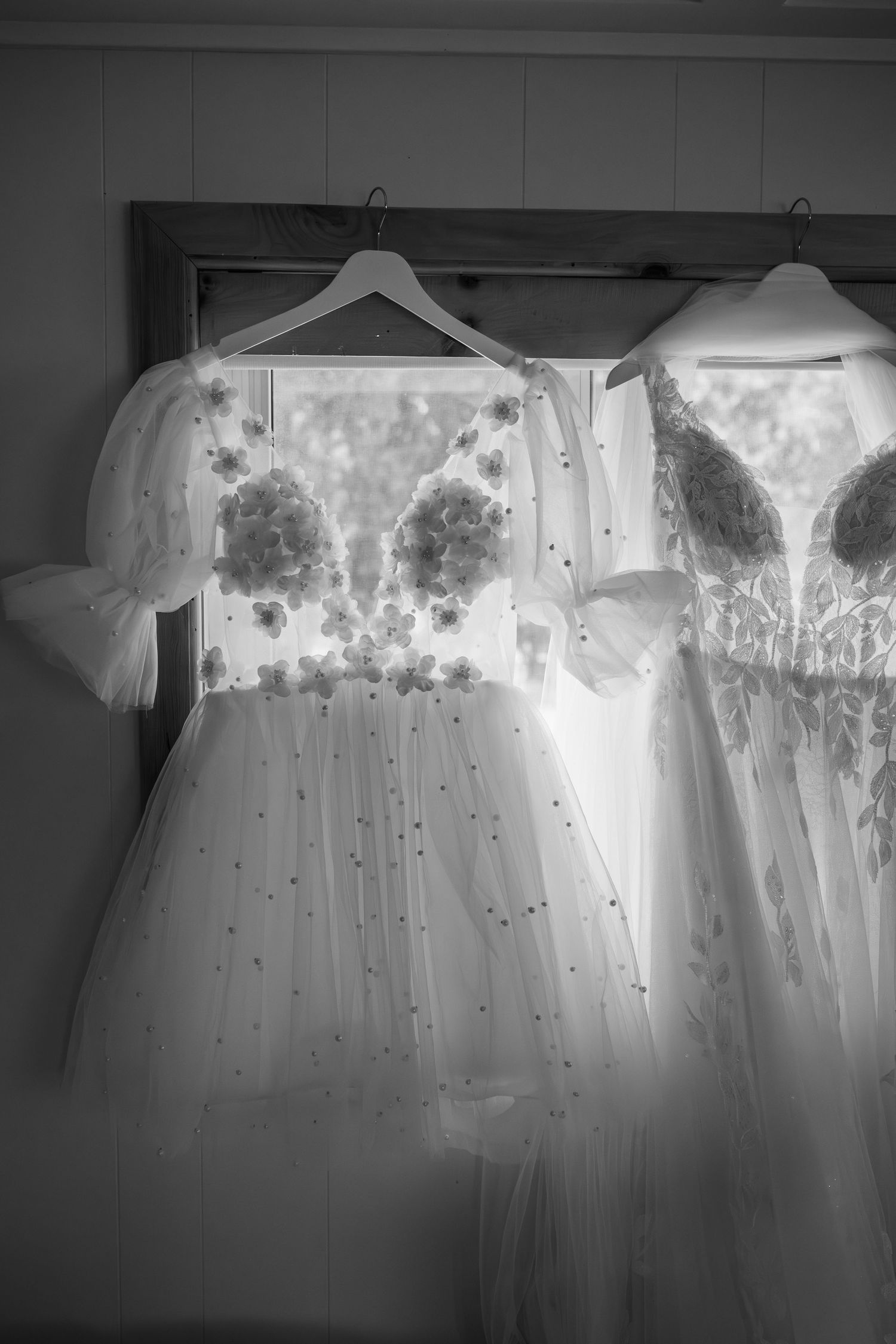 Row of ethereal white wedding dresses hanging on display with delicate floral details.
