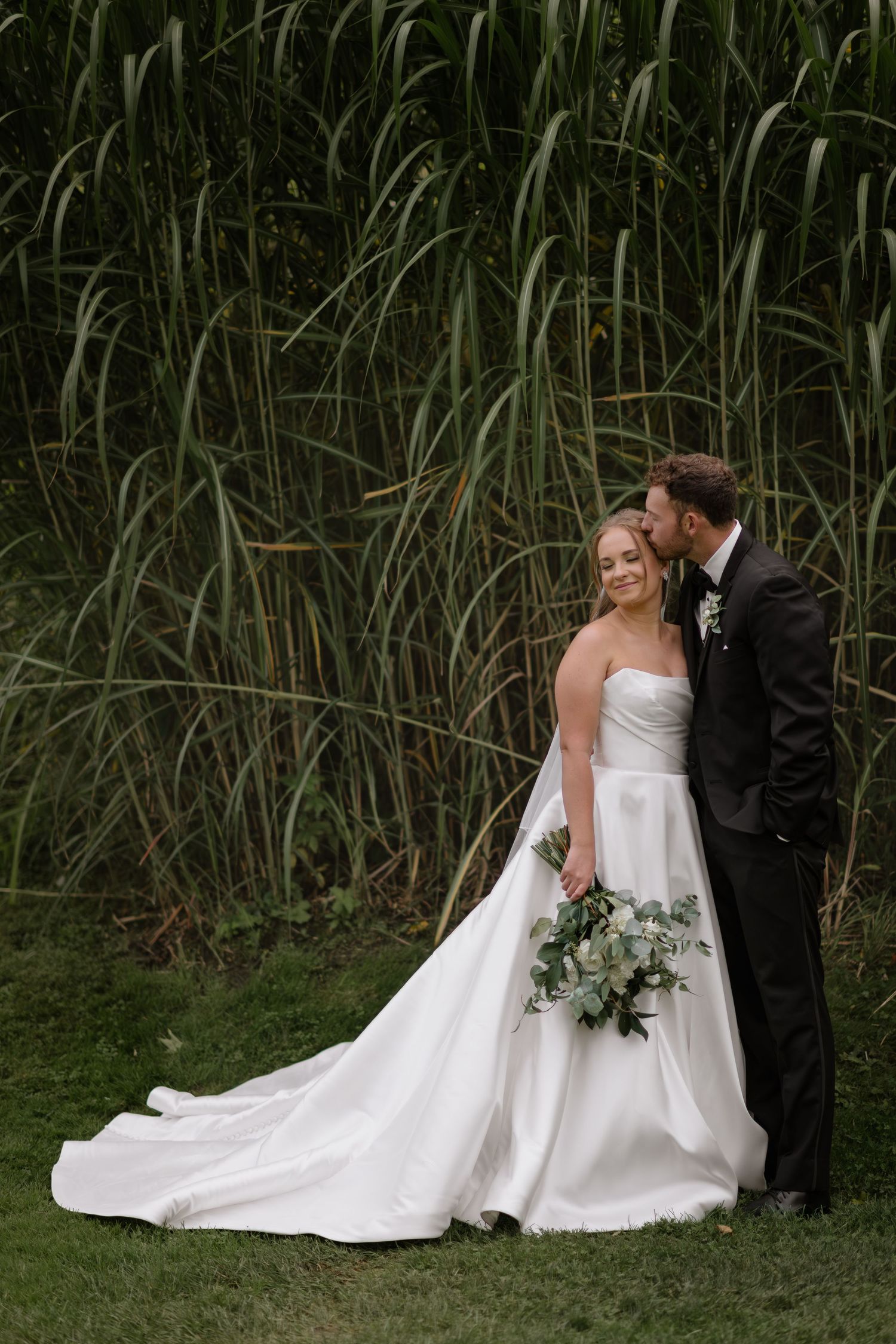 Romantic wedding couple poses together near tall grass at sunset.