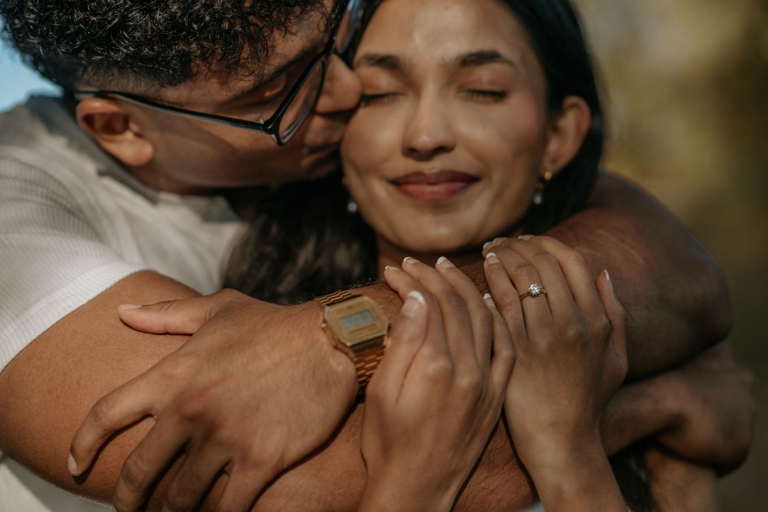 Close-up romantic photo showing hands embracing and rings in warm natural lighting.