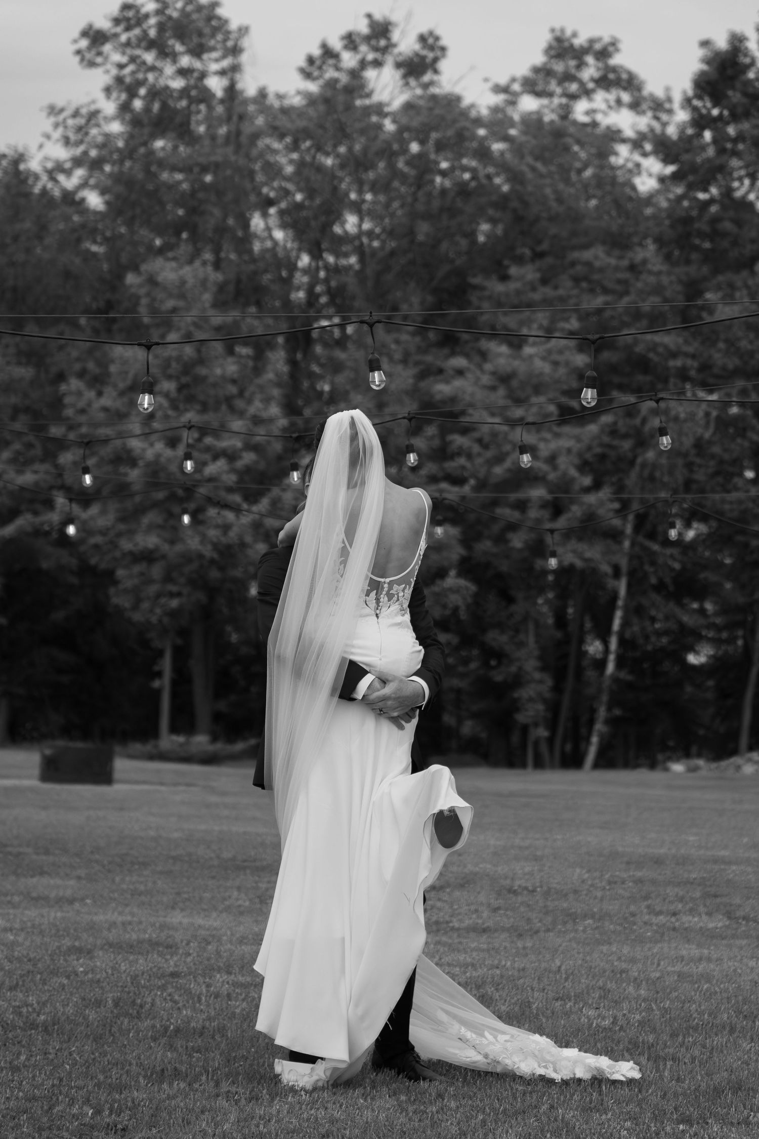 Black and white wedding photos show a couple dancing on an outdoor lawn with string lights.