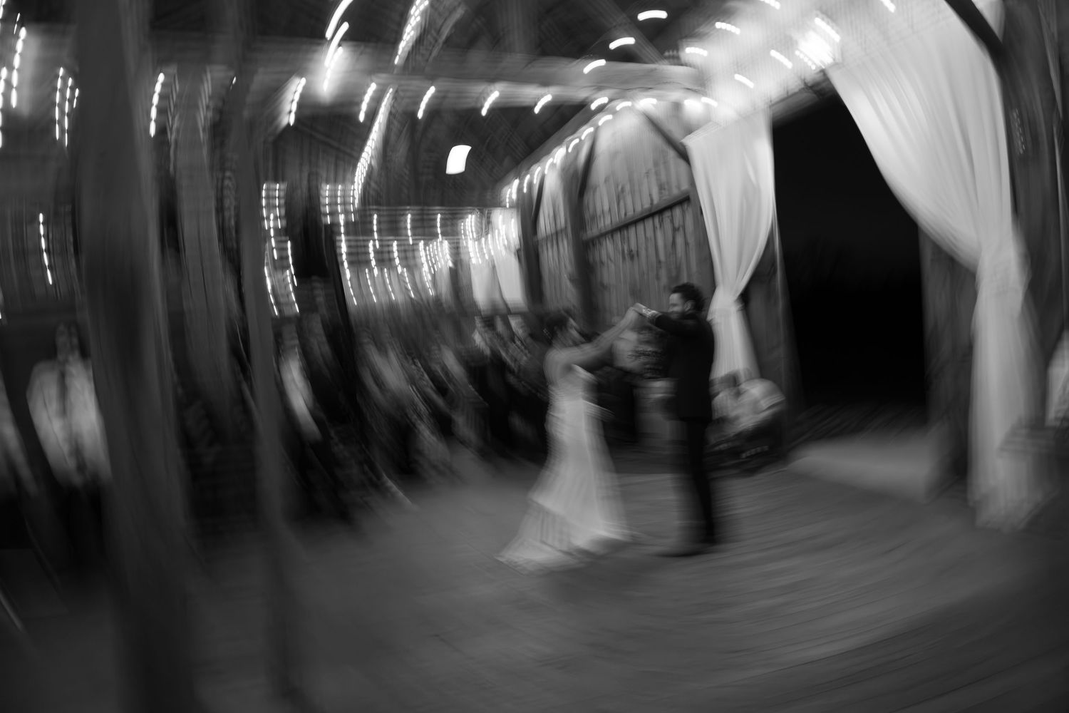 A black and white motion blur photograph shows dancers spinning on a dance floor at a wedding reception.