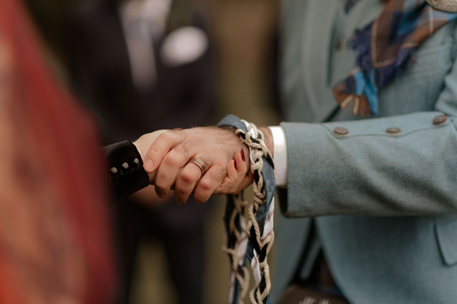 Close-up detail shot of hands wearing formal attire with plaid fabric visible in the background.