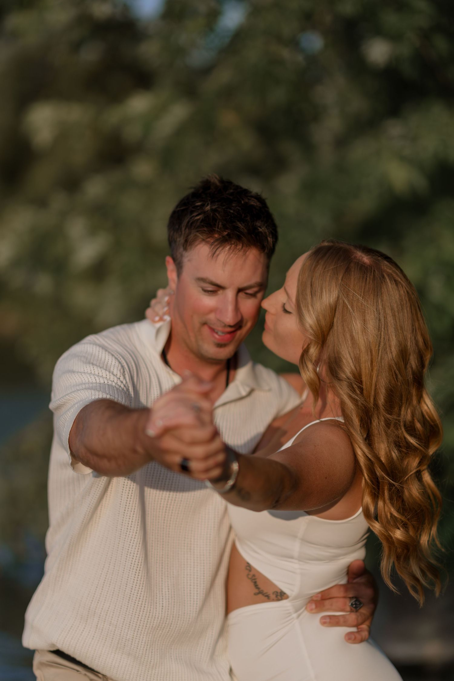 Couple in white outfits dances intimately during outdoor photo session.