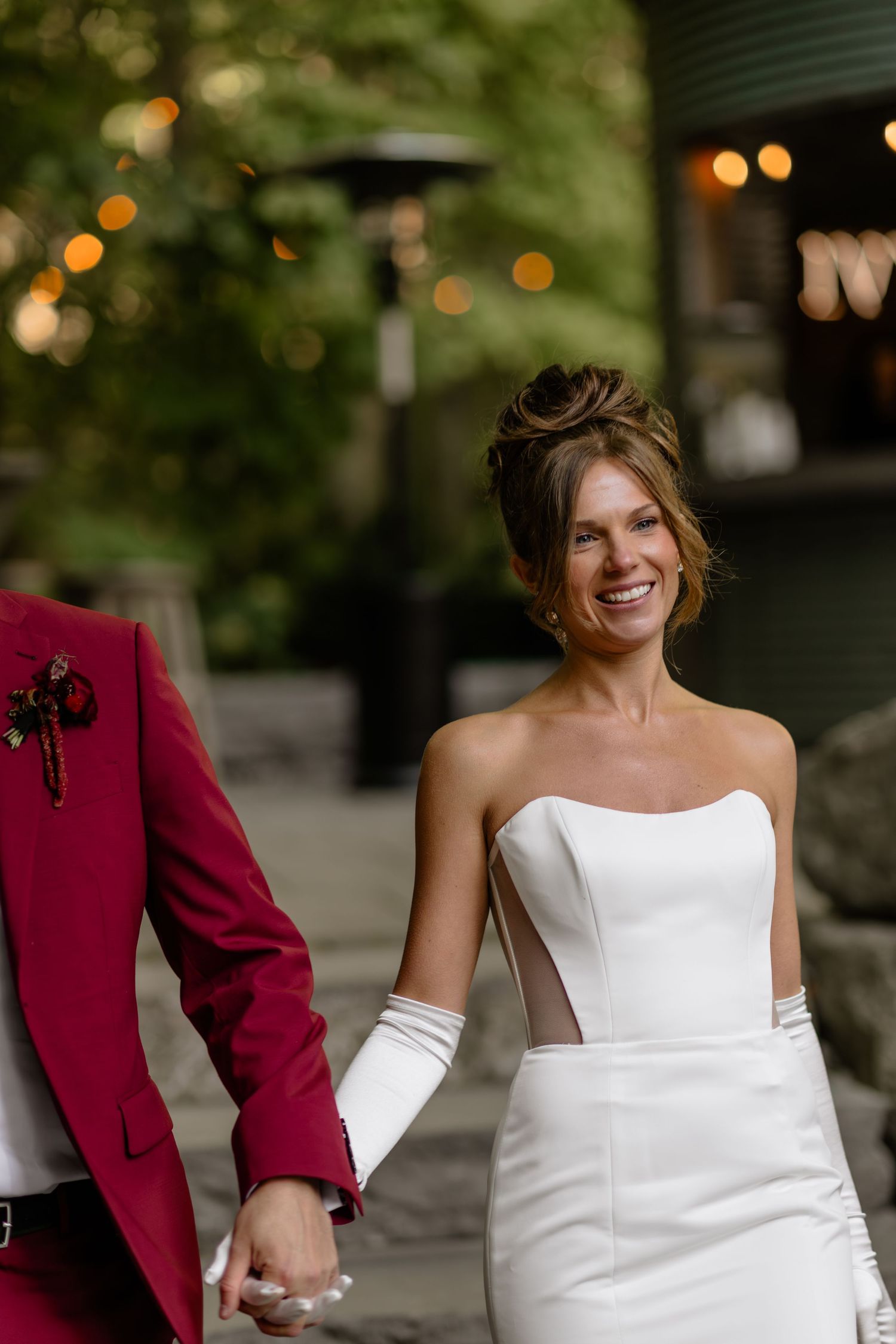 Elegant bride in strapless white gown poses with groom in burgundy suit.