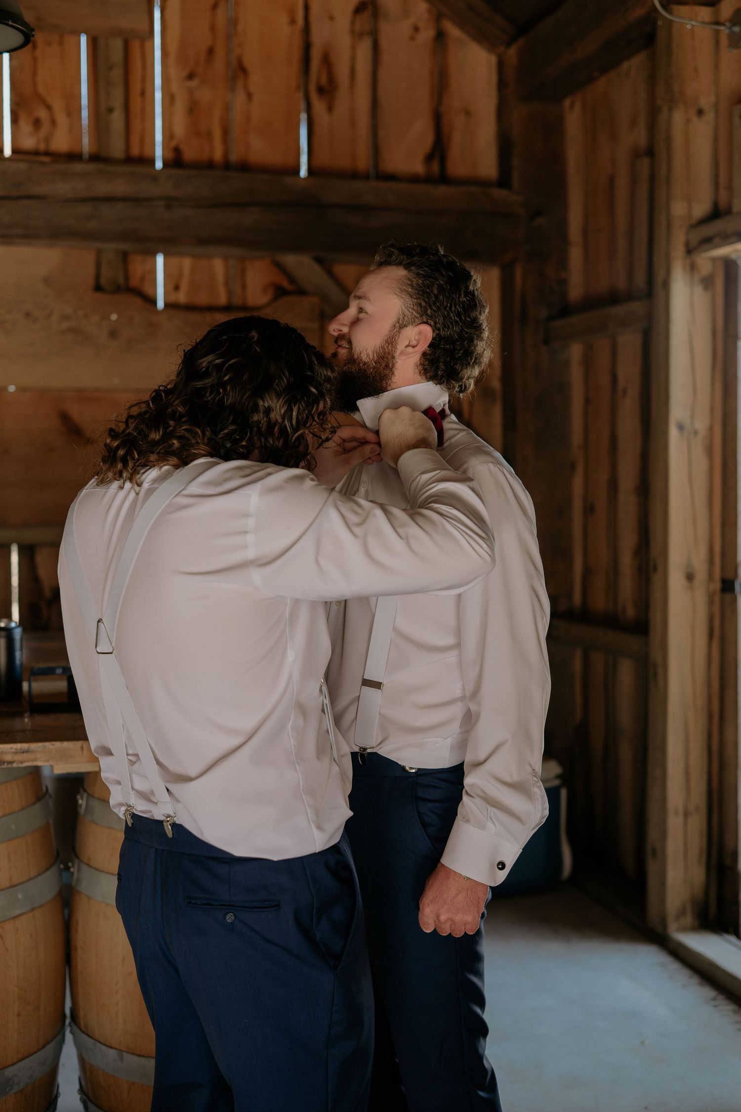 A couple in white and navy outfits share an intimate moment against a rustic wooden barn wall.