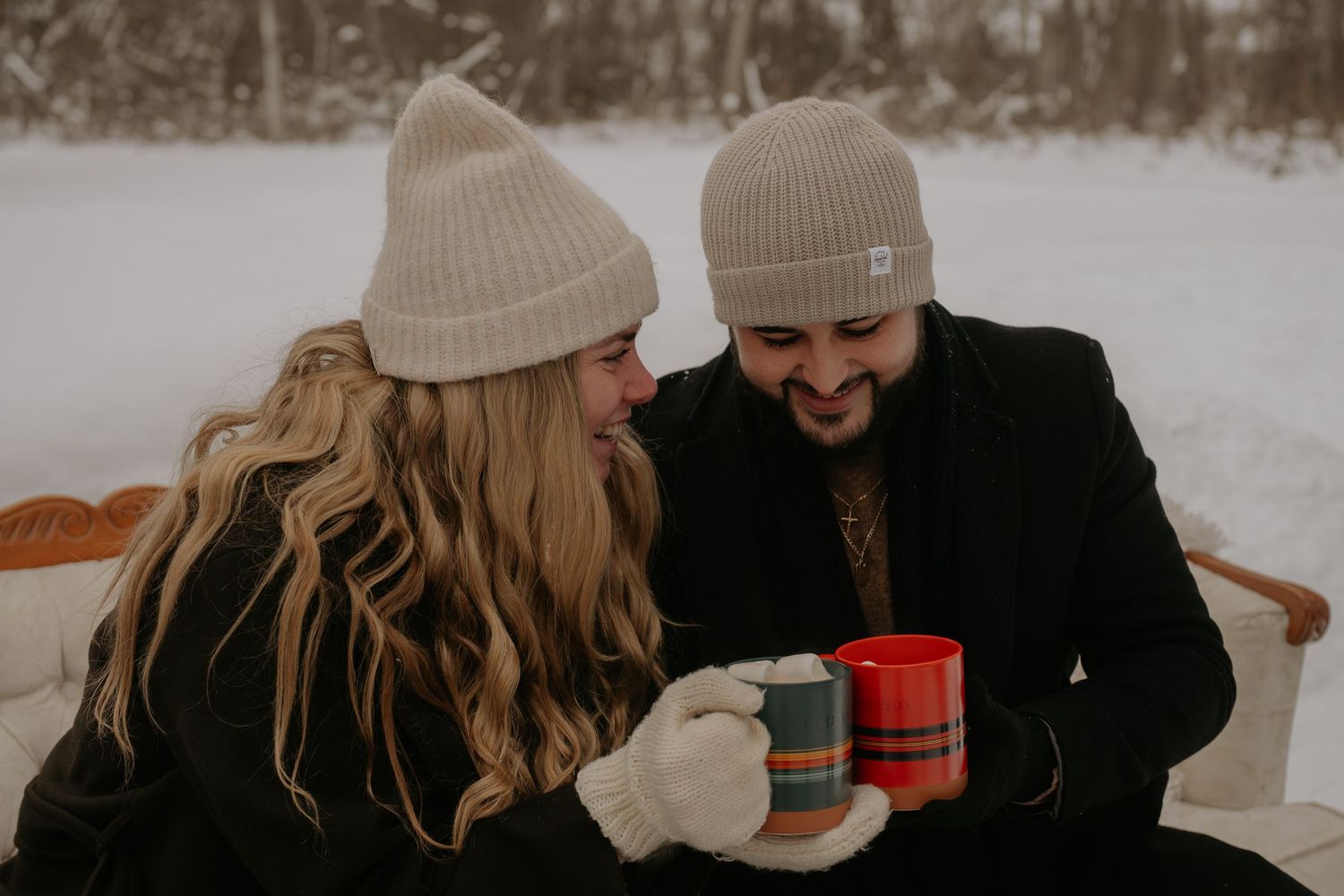 Couple wearing winter hats sharing hot drinks in the snow.