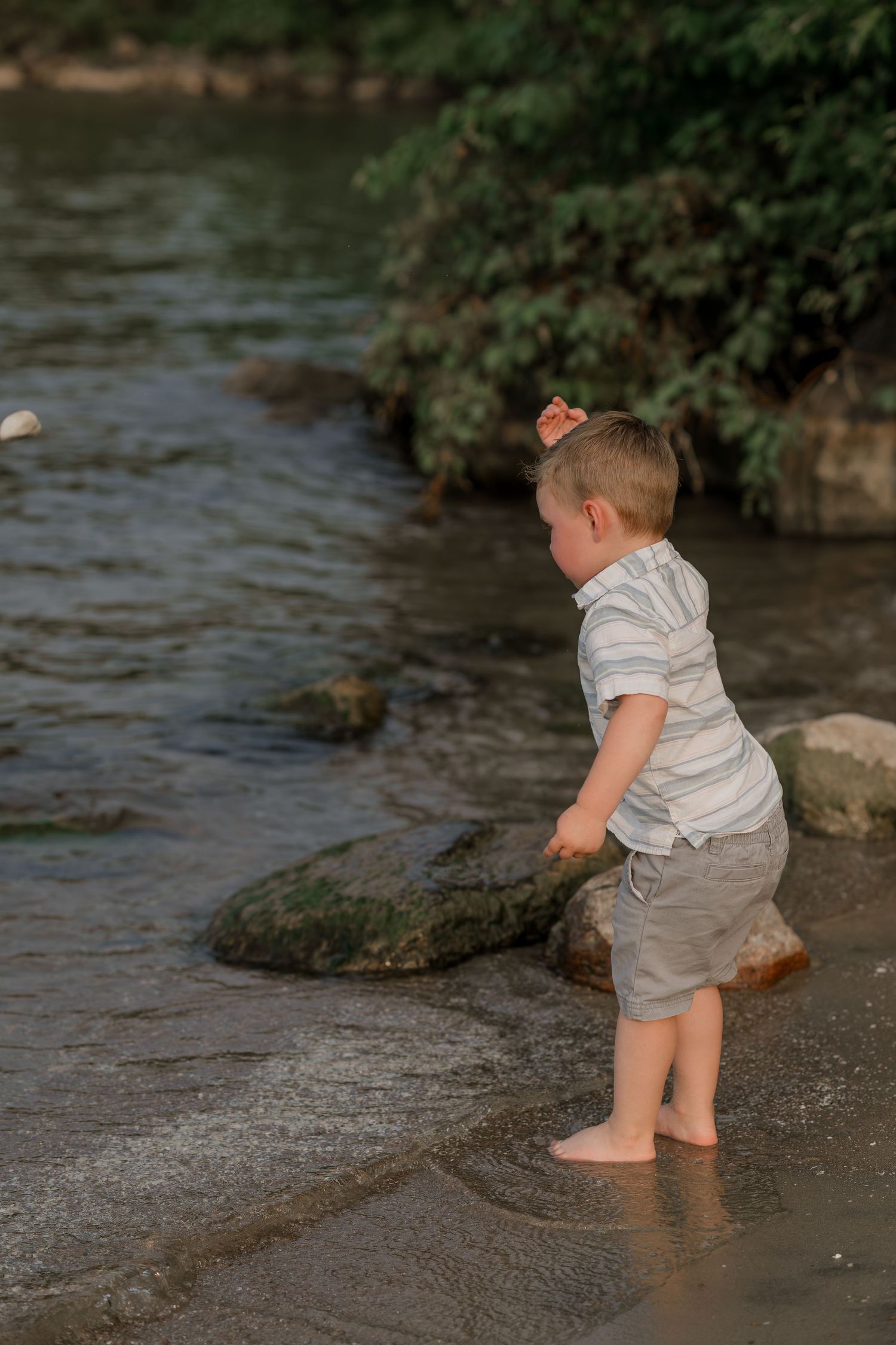 Small child in white shirt playing at the water's edge.