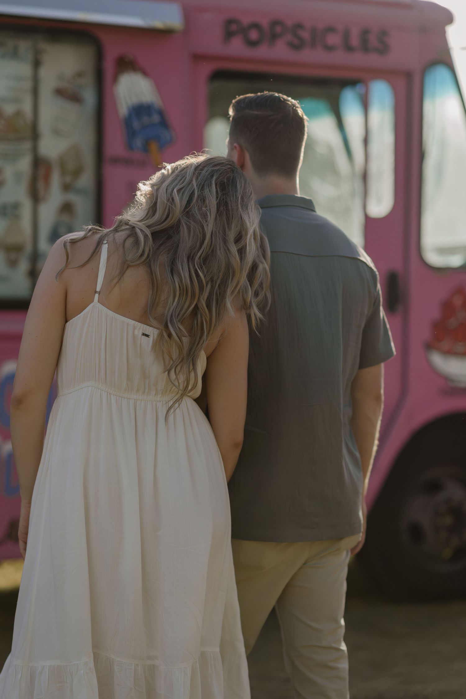 Couple walking hand in hand near a pink food truck during a casual outdoor date.