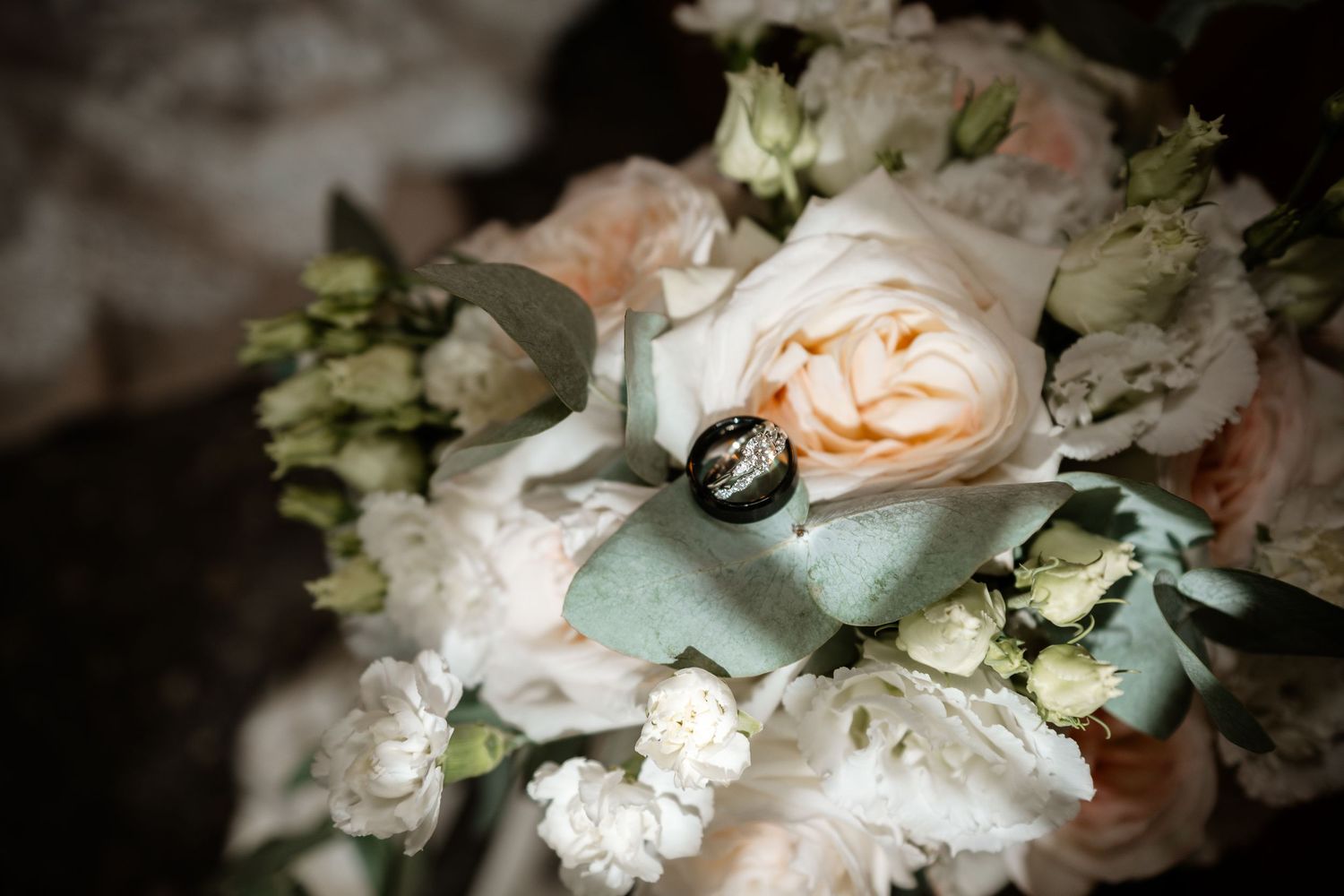Delicate floral arrangement featuring white and peach roses with eucalyptus leaves.