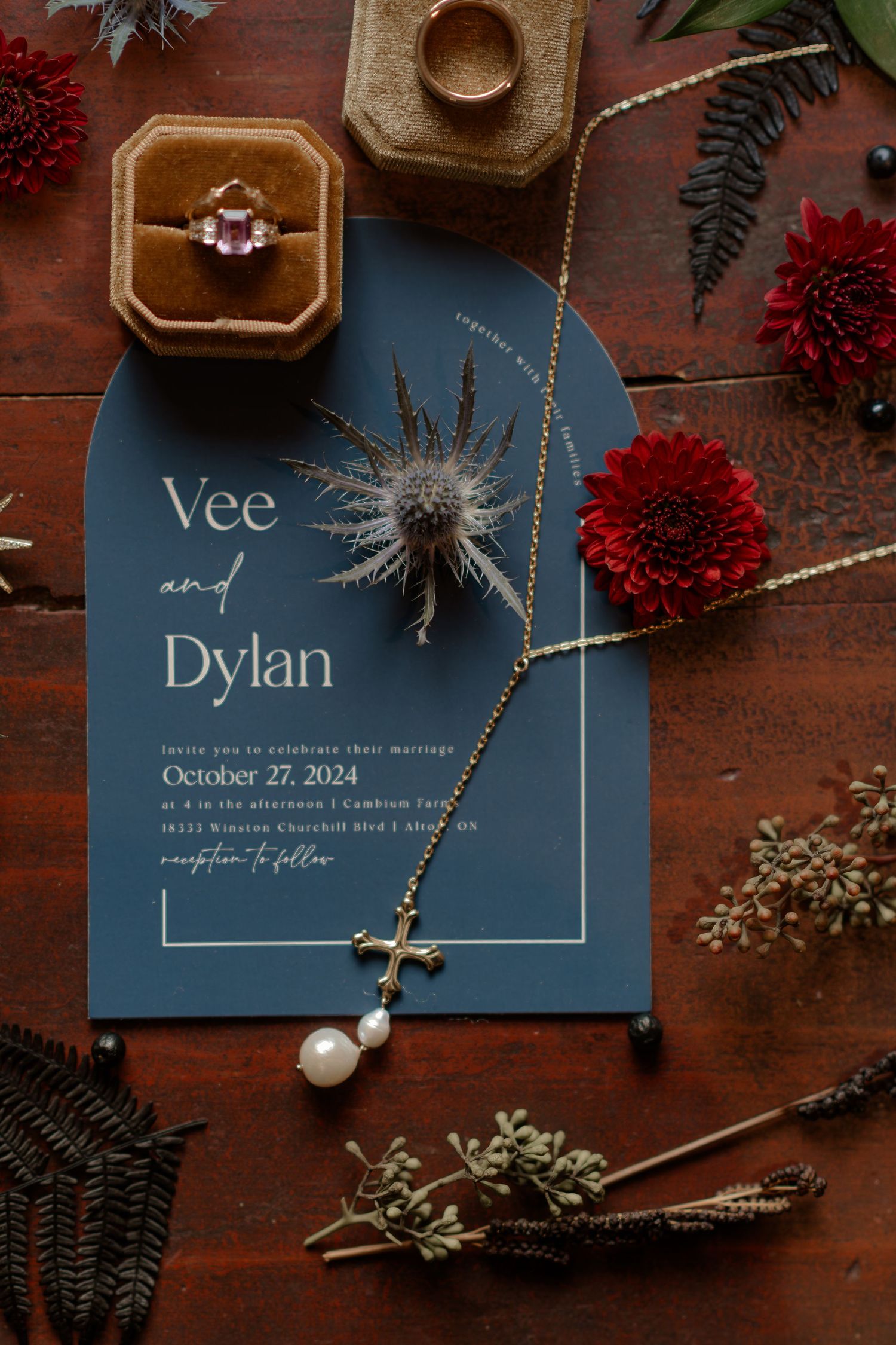 Navy blue wedding invitations with red floral accents and pearl details on a dark wooden surface.