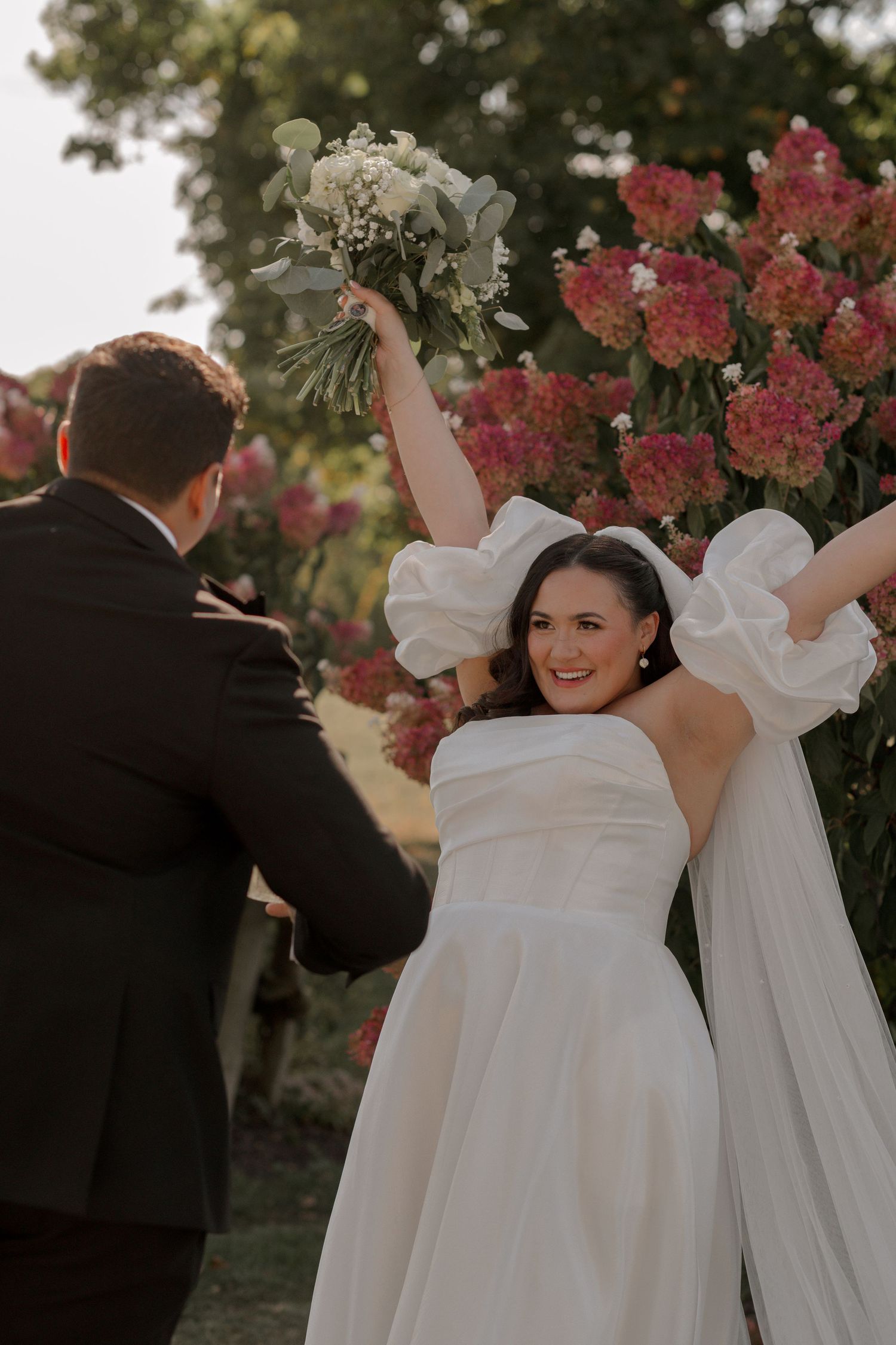 A joyful wedding celebration moment captured among blooming pink flowers in an outdoor garden setting.