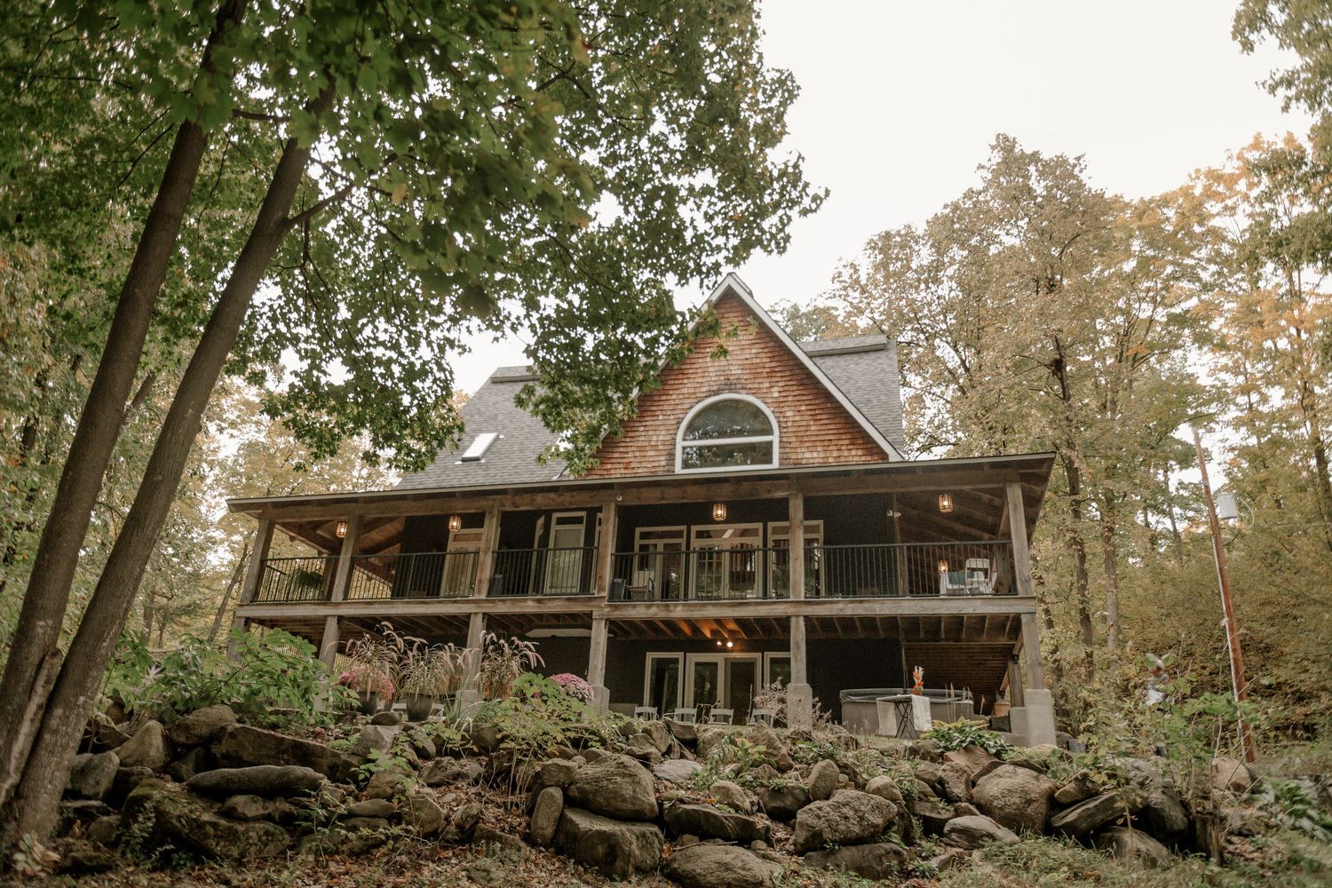 A rustic wooden cabin nestled among trees with a wraparound porch and large windows overlooking the forest.