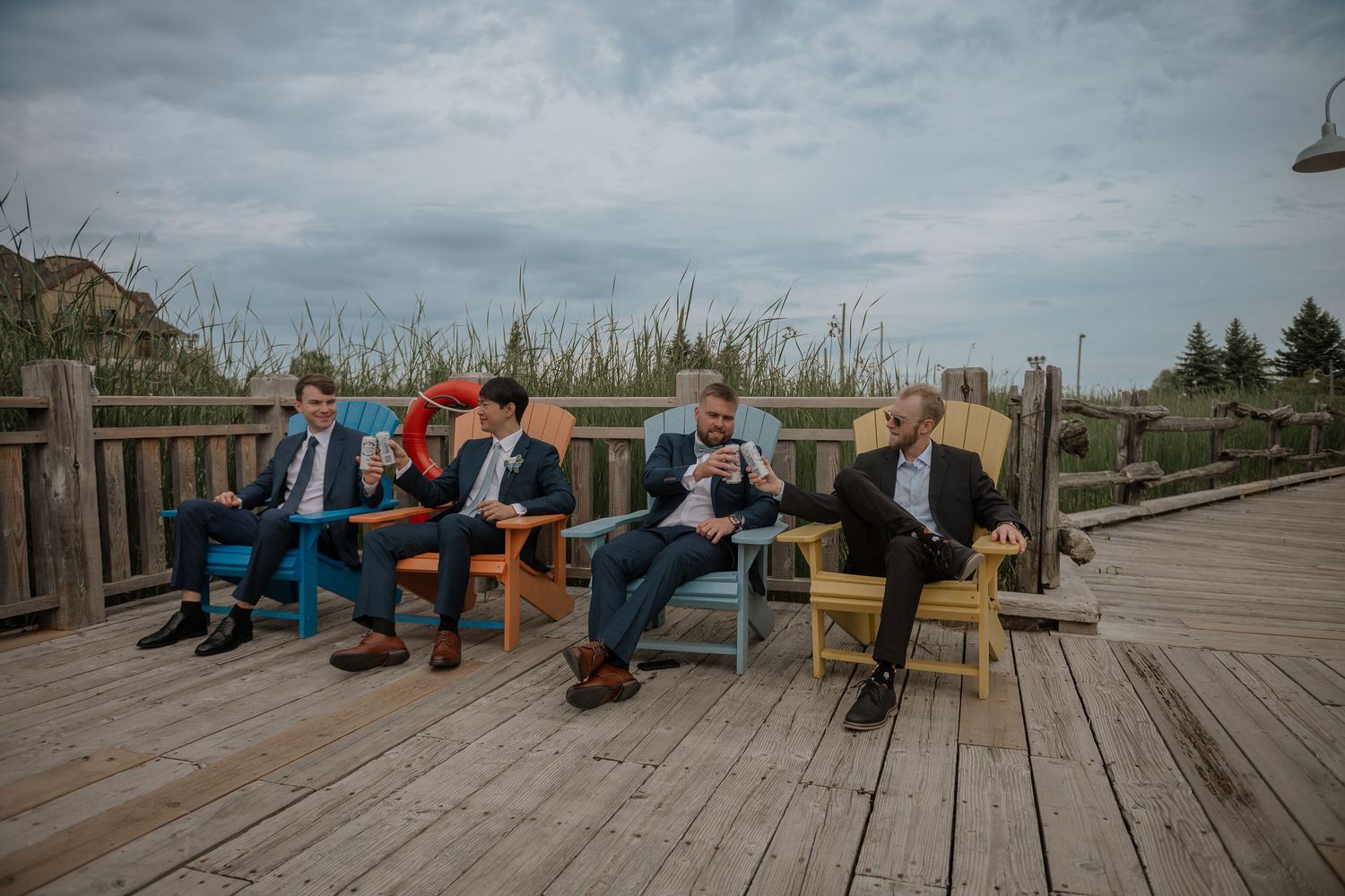 Wedding party members relax on wooden deck chairs against a scenic outdoor backdrop.