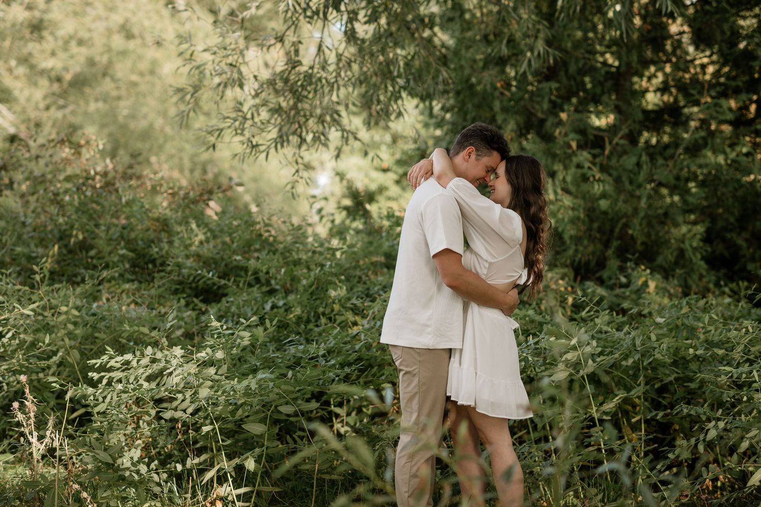 Couple sharing a romantic embrace in a sunlit garden setting.