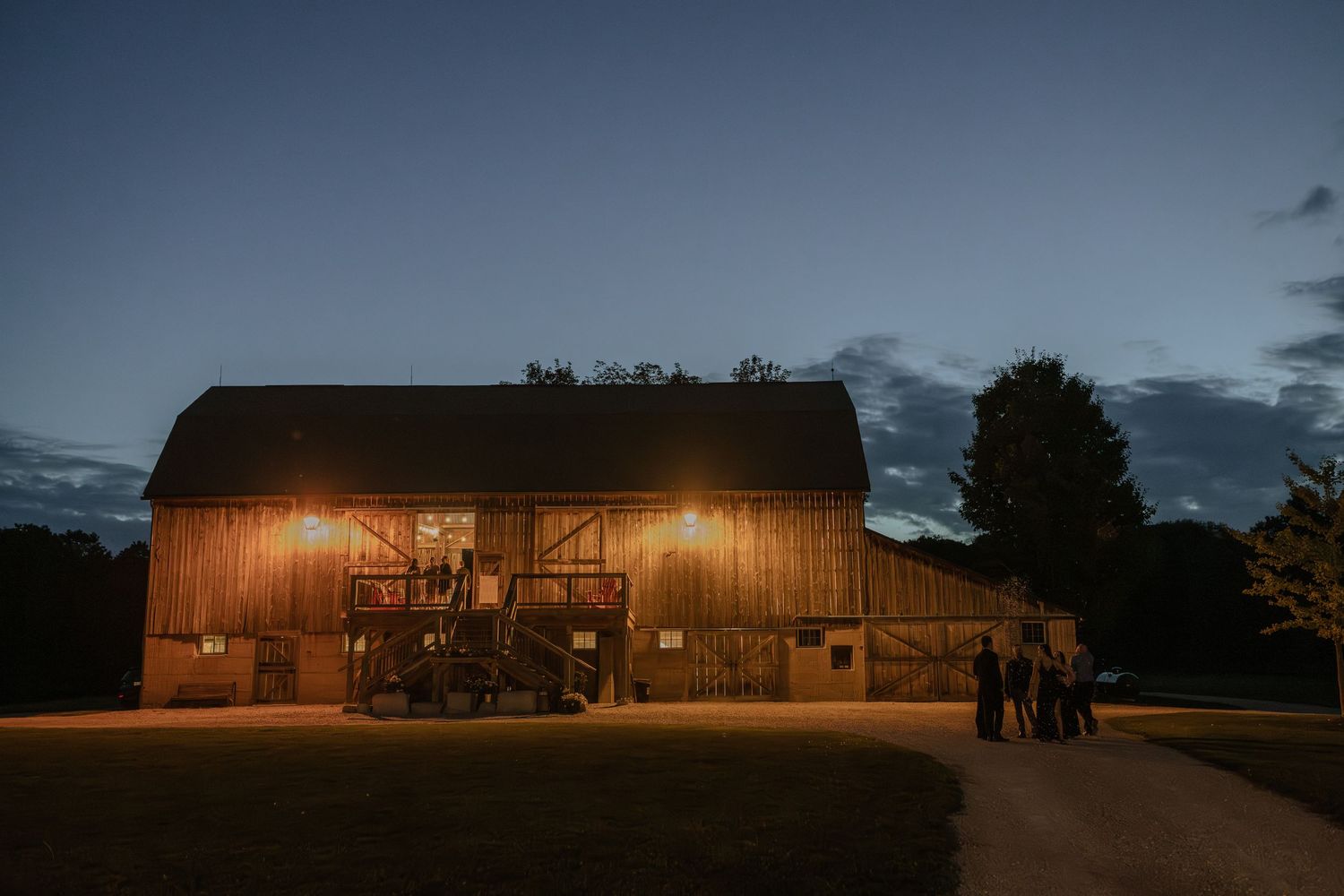 Rustic wooden barn venue illuminated at dusk during an outdoor wedding celebration.