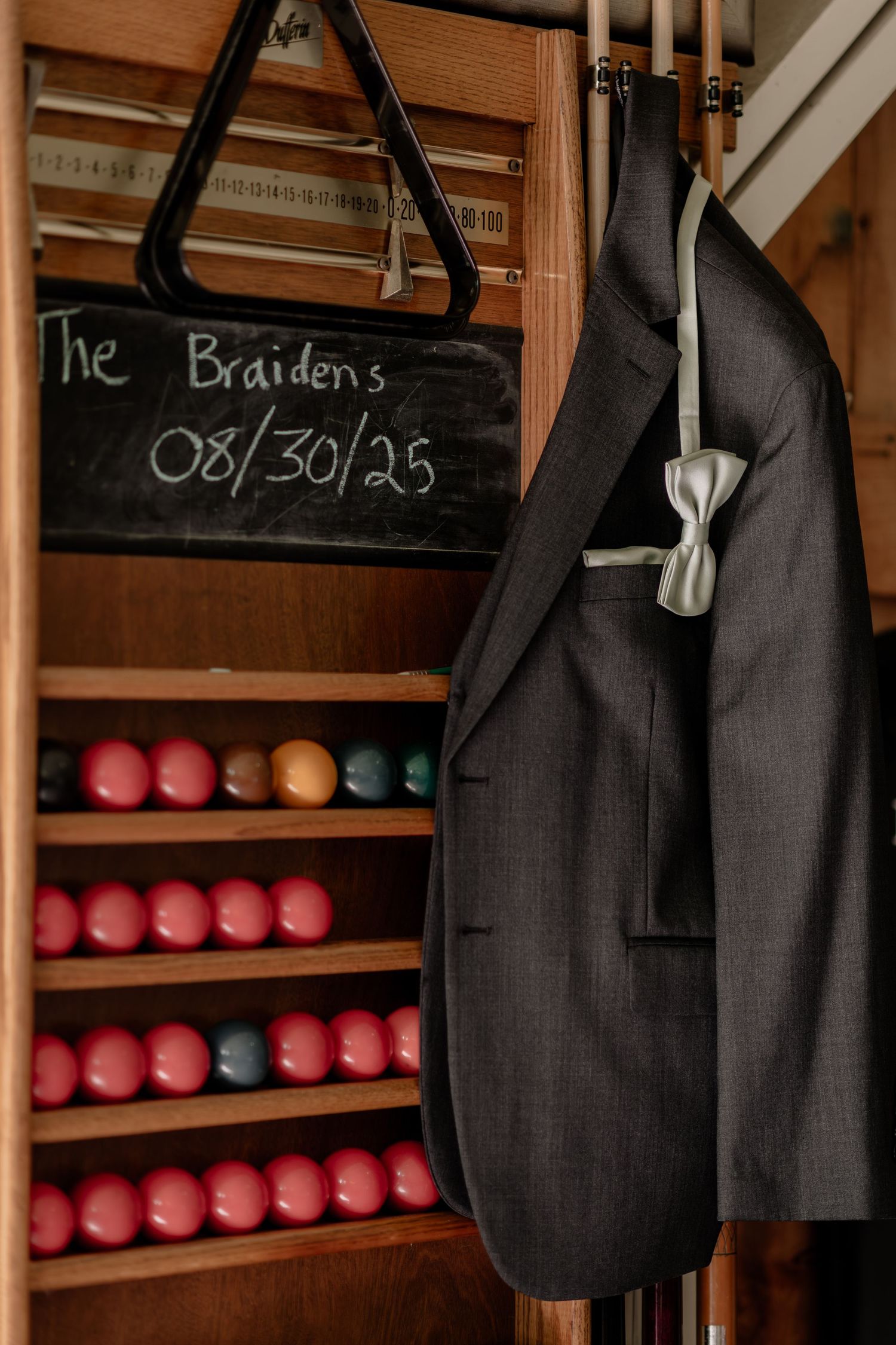 Row of dark suit jackets hanging in a rustic wooden closet with red bowling balls displayed below.