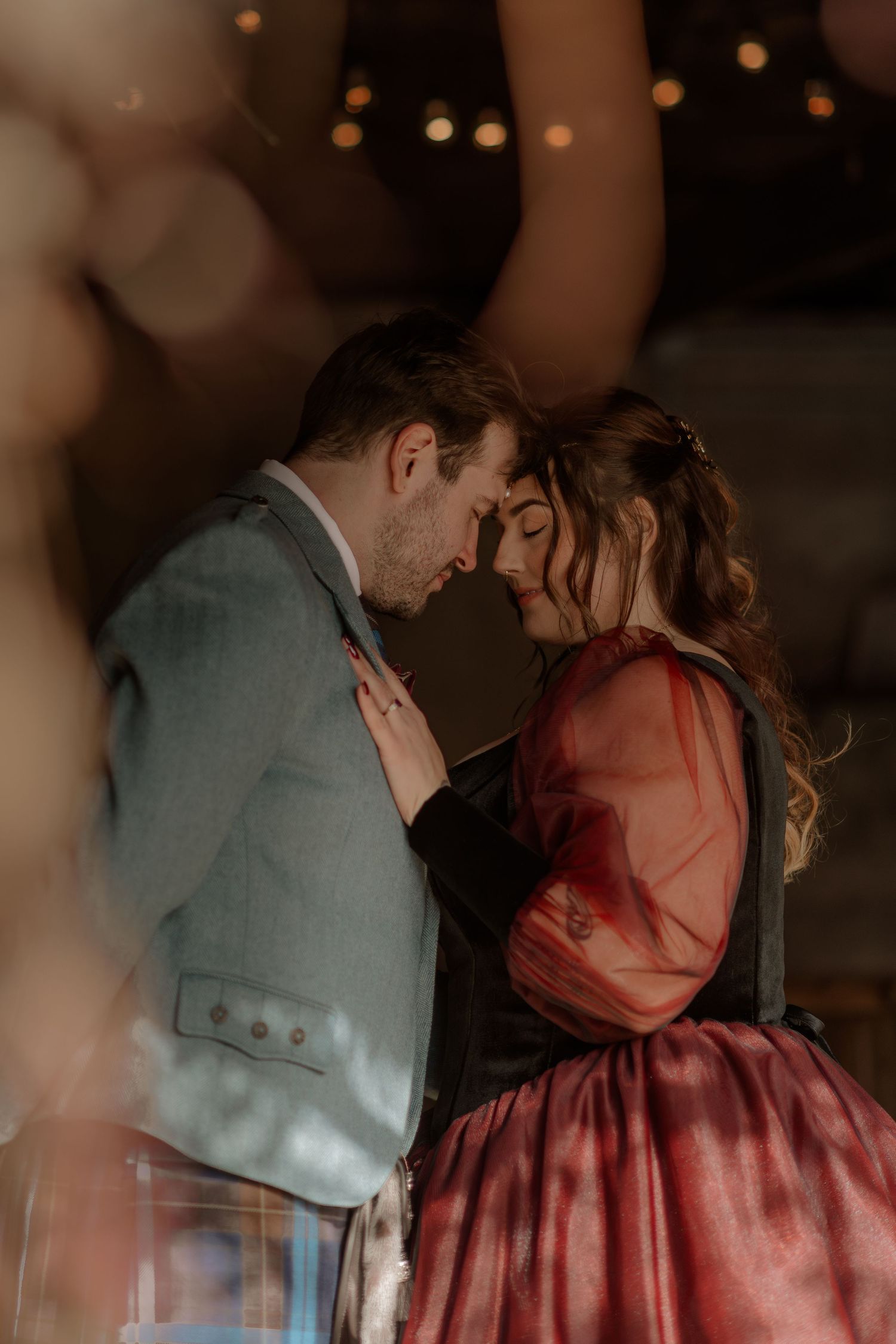 A romantic couple in formal attire sharing an intimate moment with soft bokeh lights in the background.