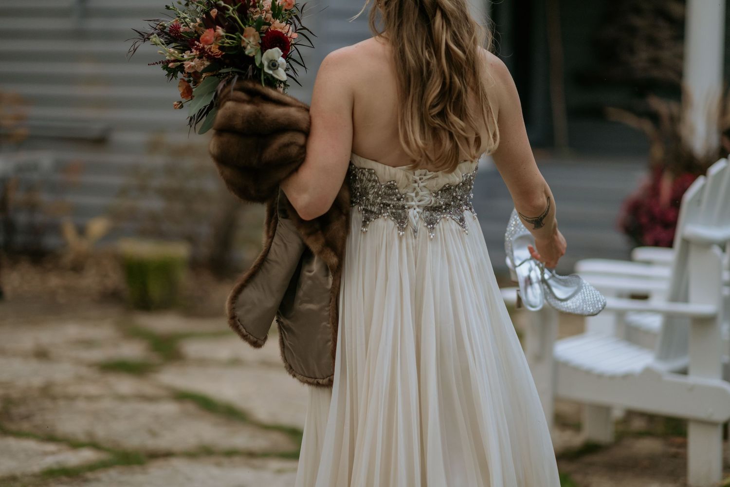 A bride in a flowing white dress holds a bouquet while walking through a rustic outdoor setting.