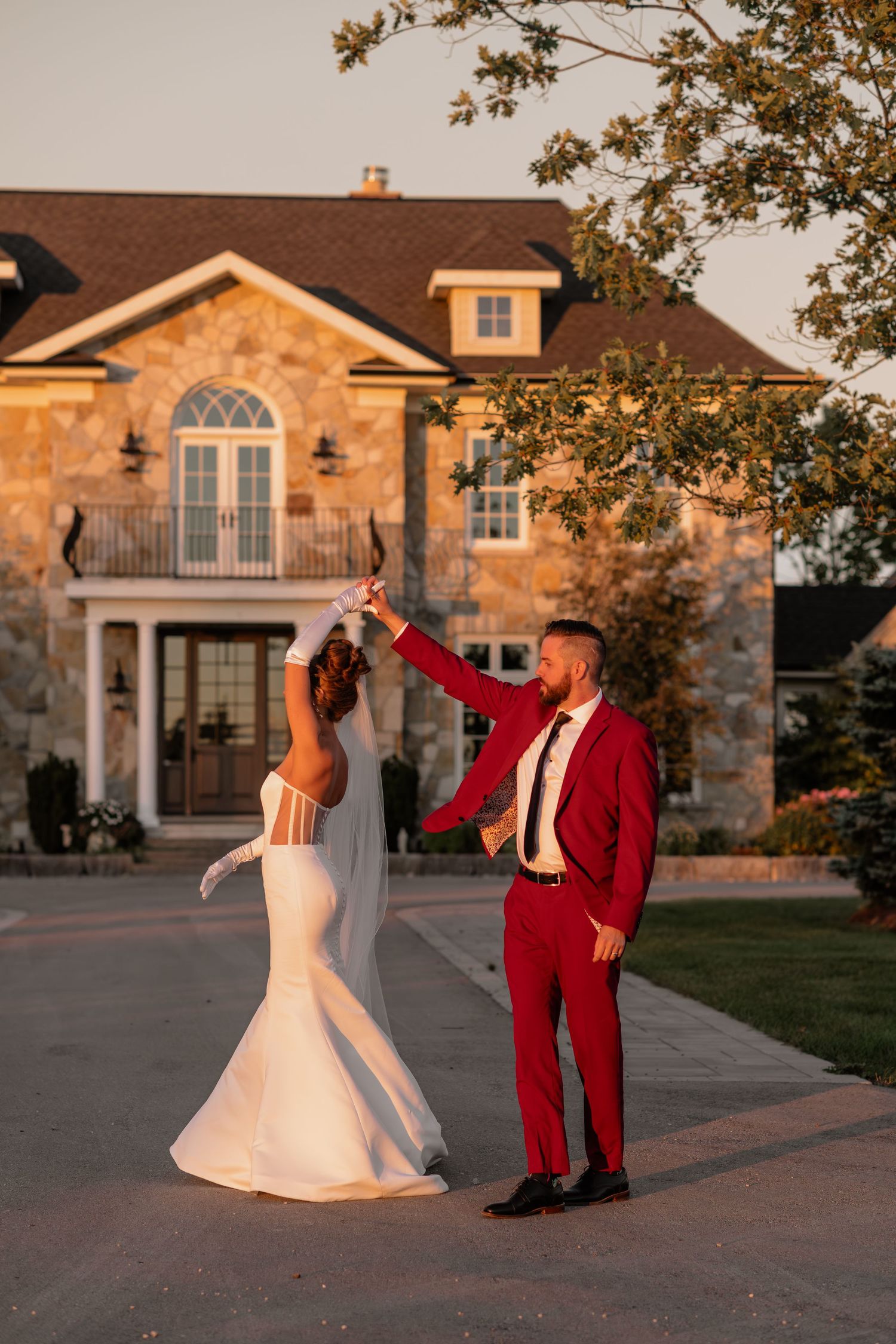 Playful wedding couple dances together at sunset in front of a stone house.