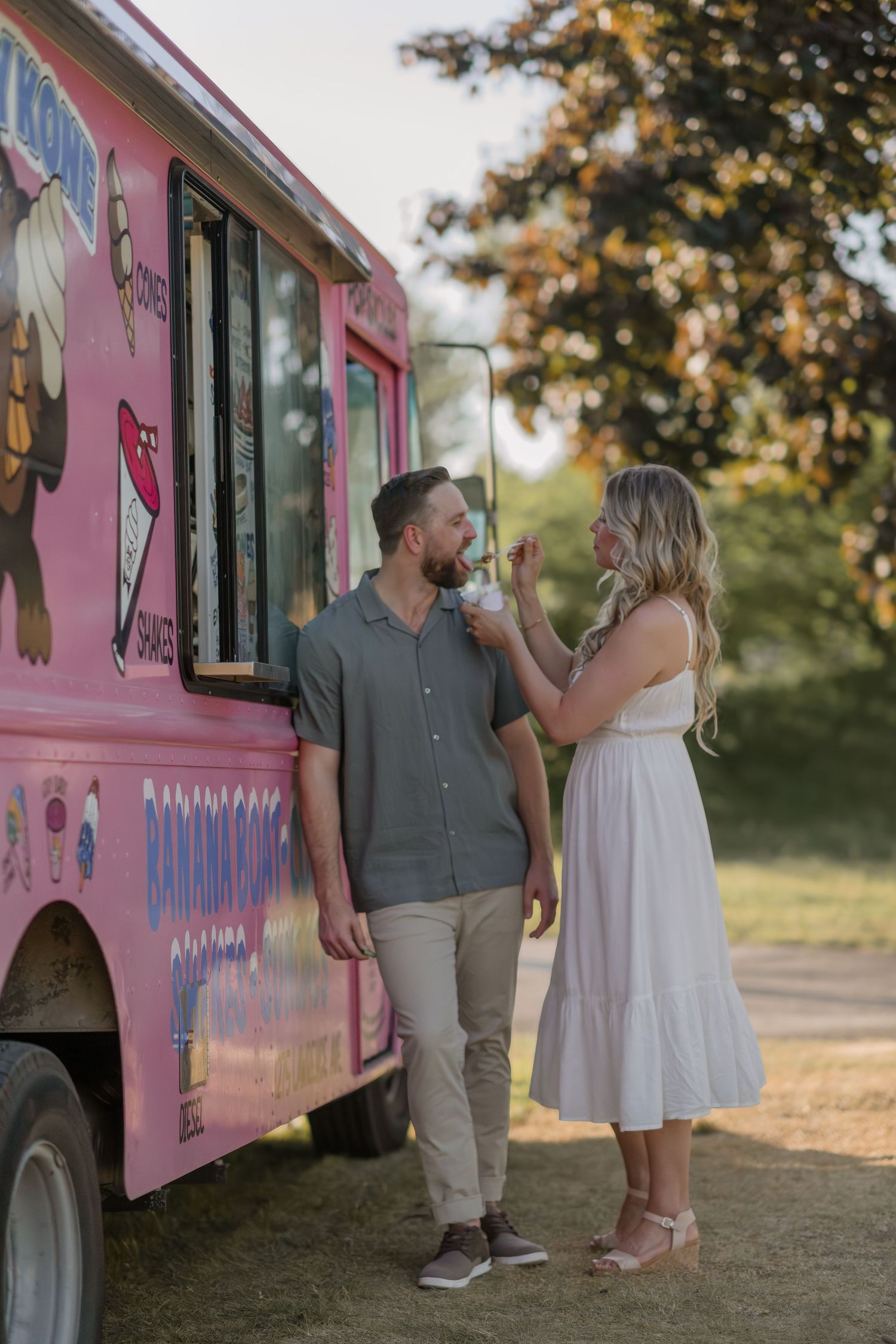 Couple enjoying milkshakes together beside a pink food truck on a sunny afternoon.