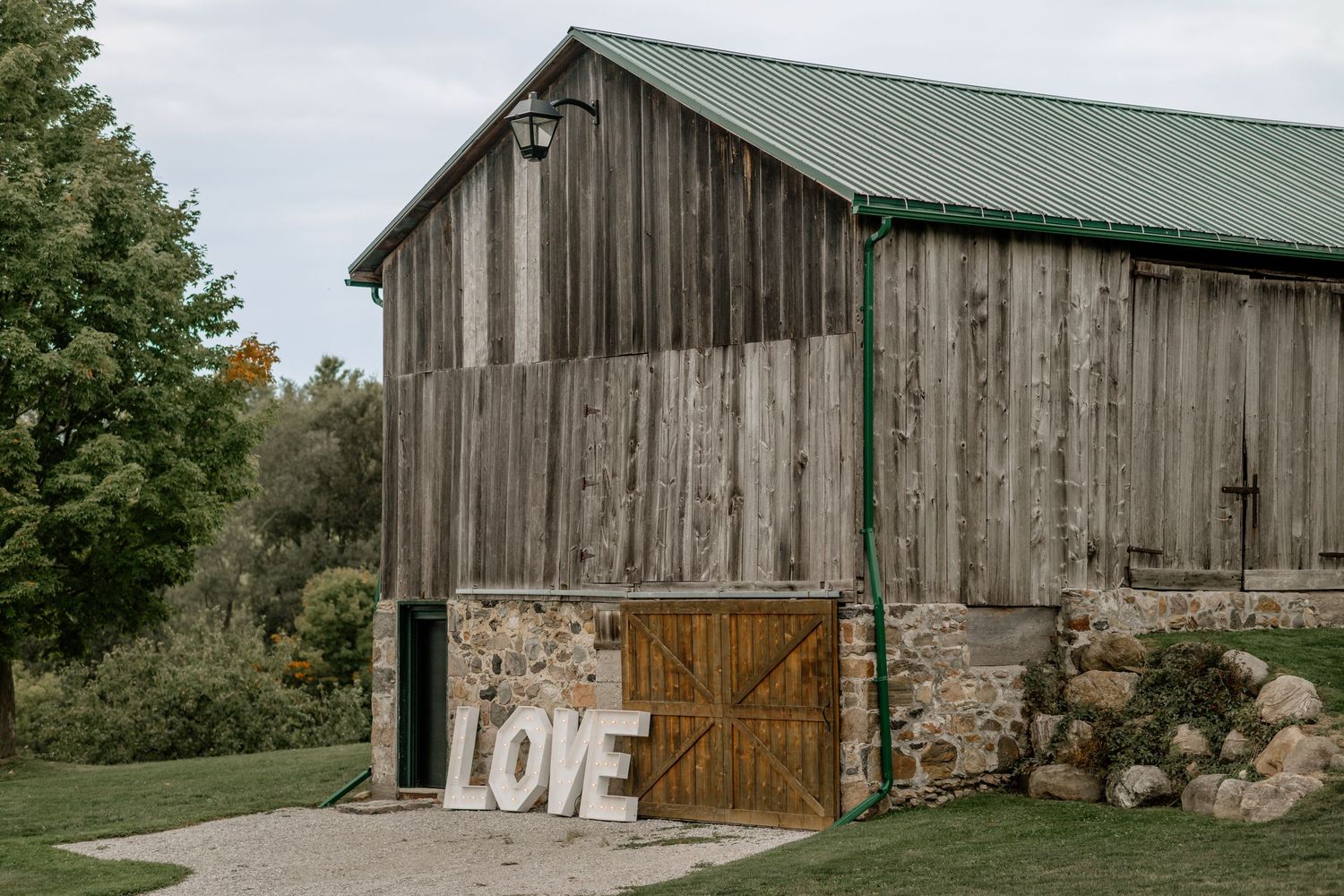 Rustic wooden barn with green metal roof in a countryside setting.