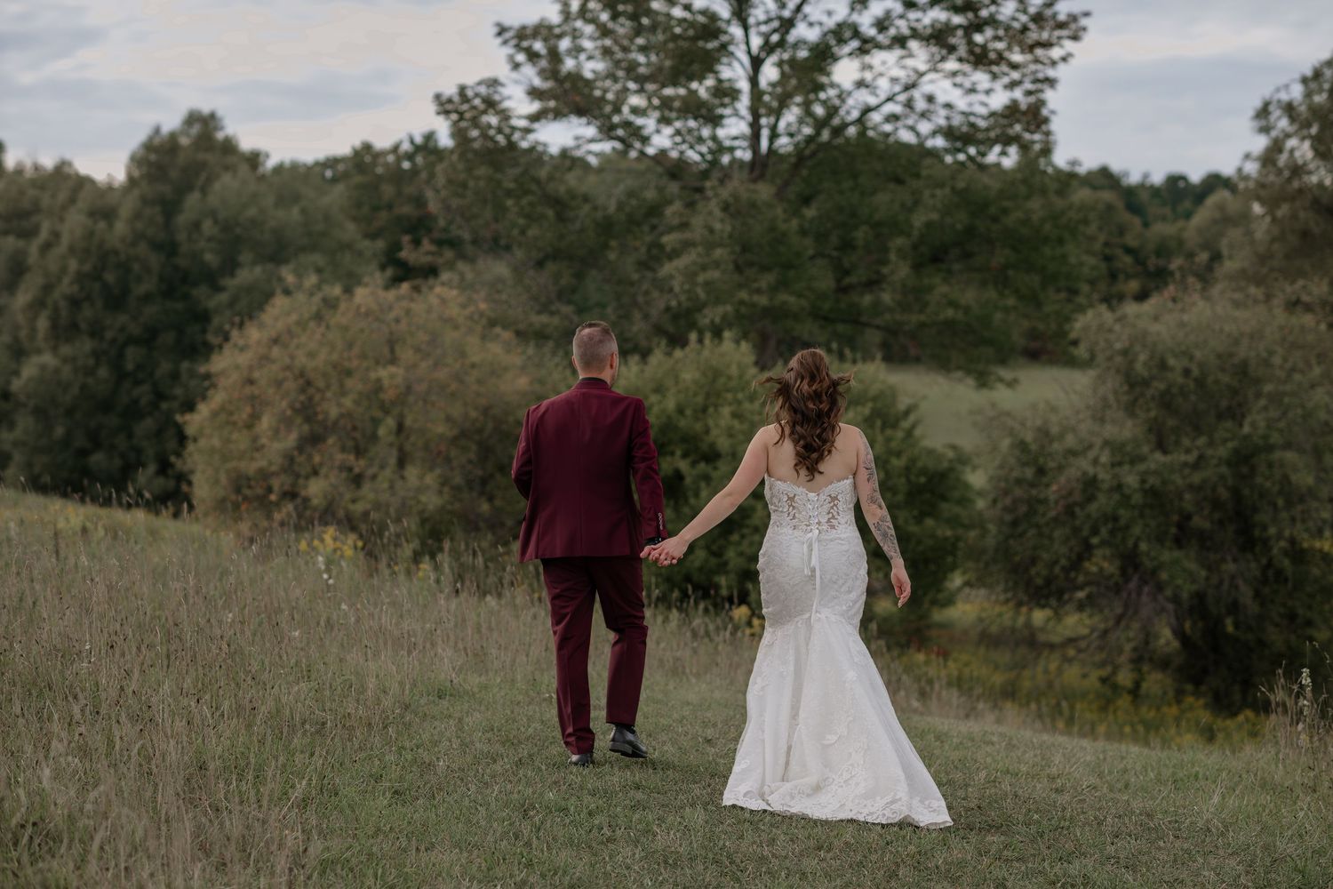 Couple walks through a scenic meadow during golden hour wedding photoshoot.