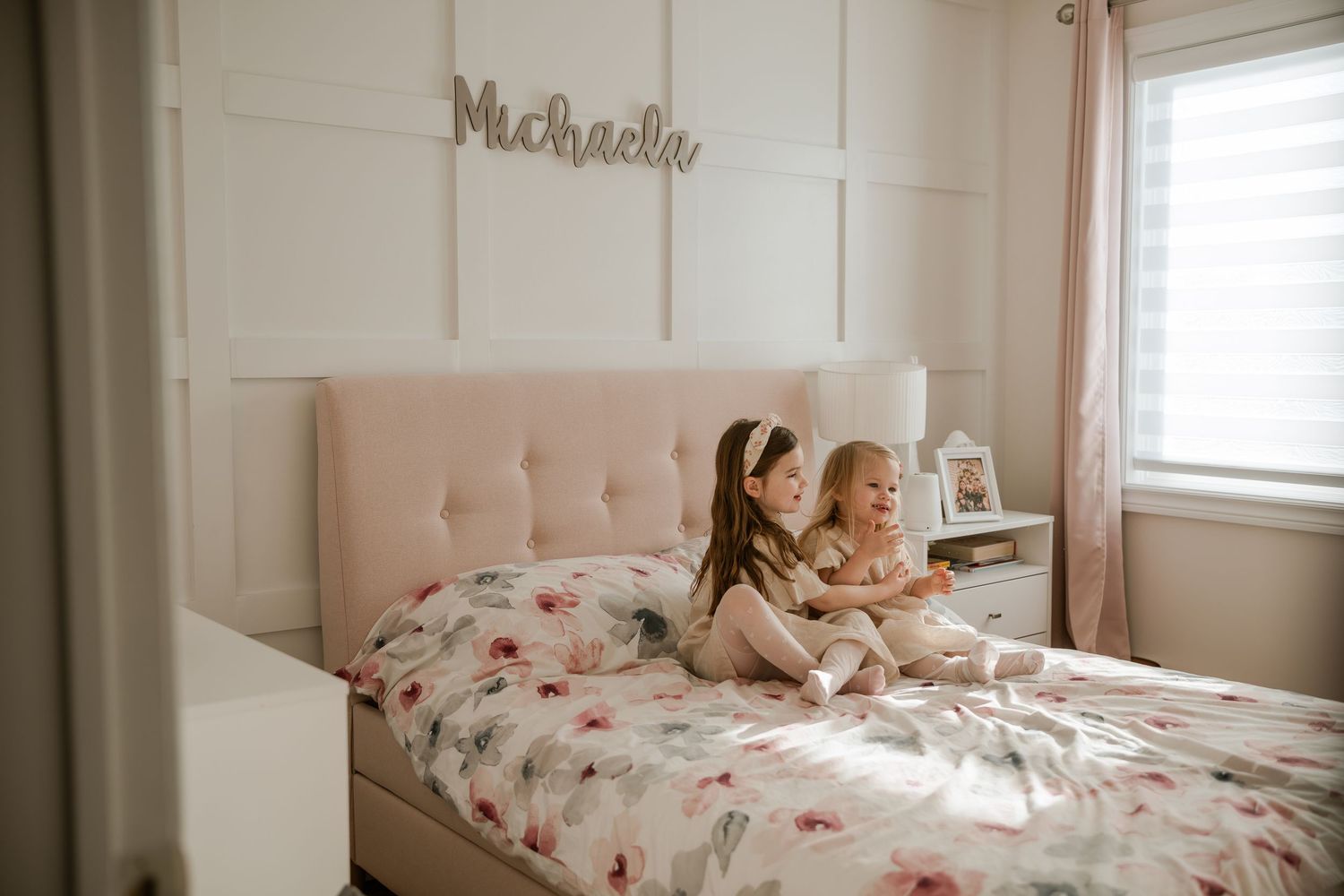 Child resting on floral bedding in sunlit bedroom.