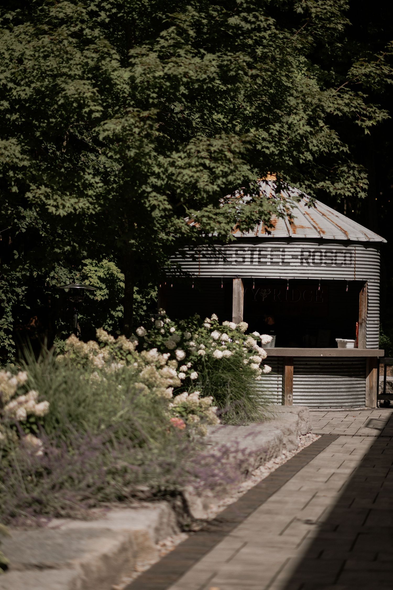 Modern steel and wood structure with 'Steel Rose' signage surrounded by garden landscaping.