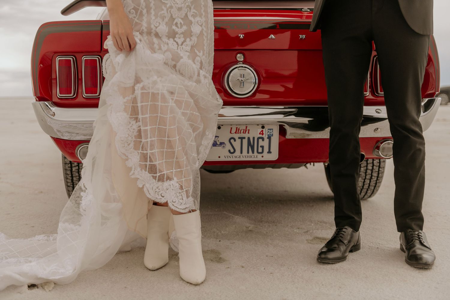 A bride and groom stand in front of vintage red cars during their wedding photo session.