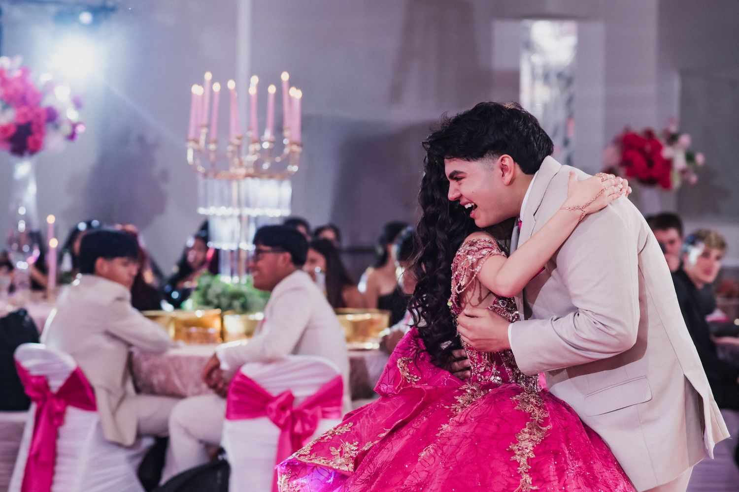 Couple sharing a romantic embrace at a formal event, woman in red gown, man in white suit, elegant banquet hall.