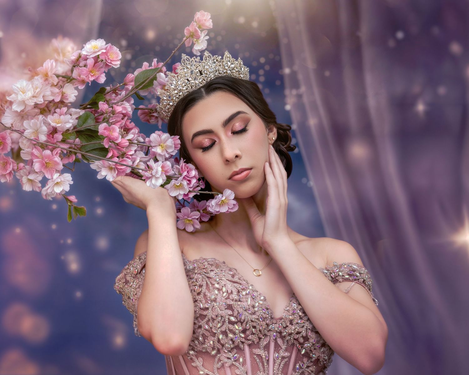 A young woman in a pink lace gown and crystal crown holds cherry blossoms against a dreamy purple bokeh background.