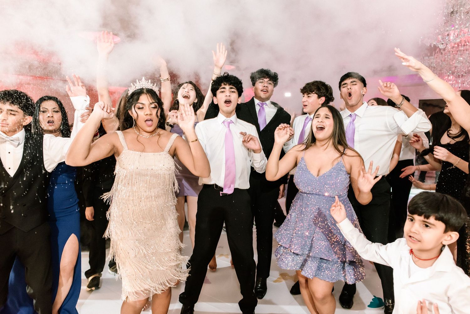 Teens celebrate at Sweet 16 party dancing energetically with smoke effects in formal attire.