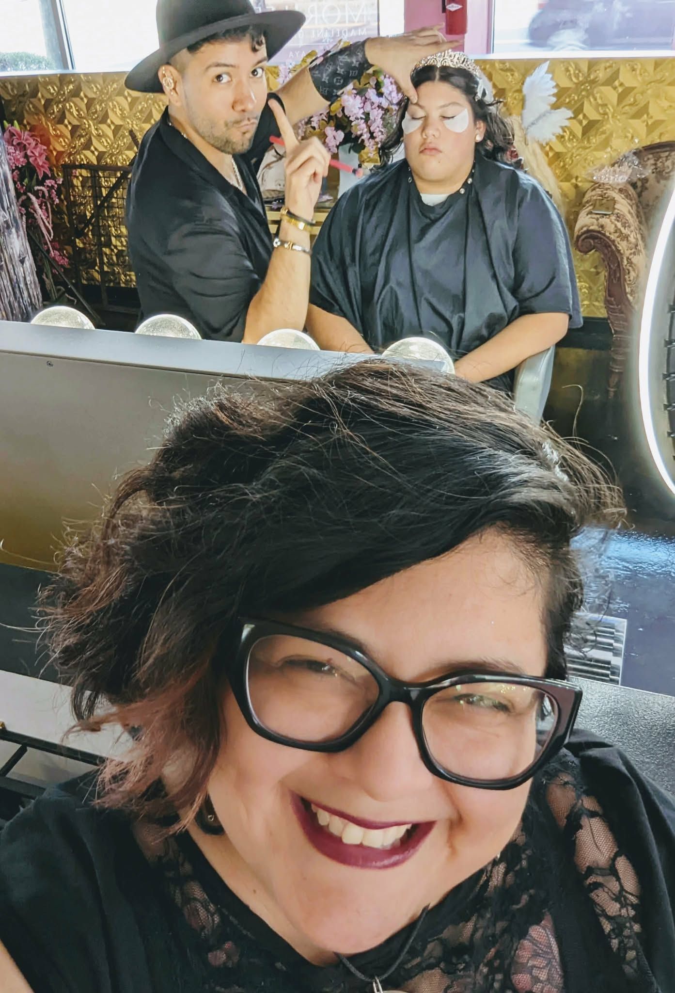 Claudia Ruiz (Raven), photographer at taken by raven takes a selfie at a salon while Chris Huertas works on another client's hair.