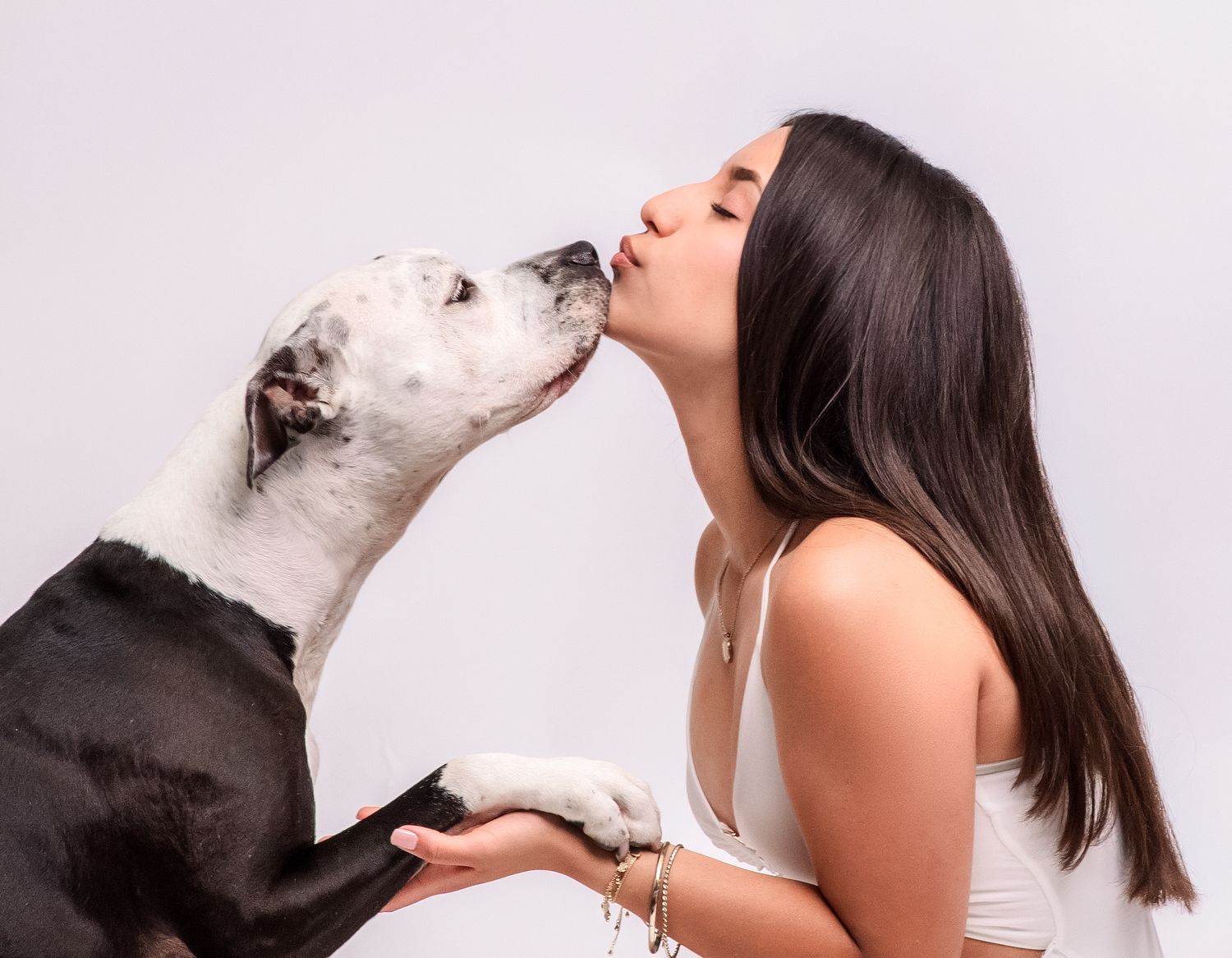 A young woman shares a kiss with her black and white dog while gently cradling its face in her hands.