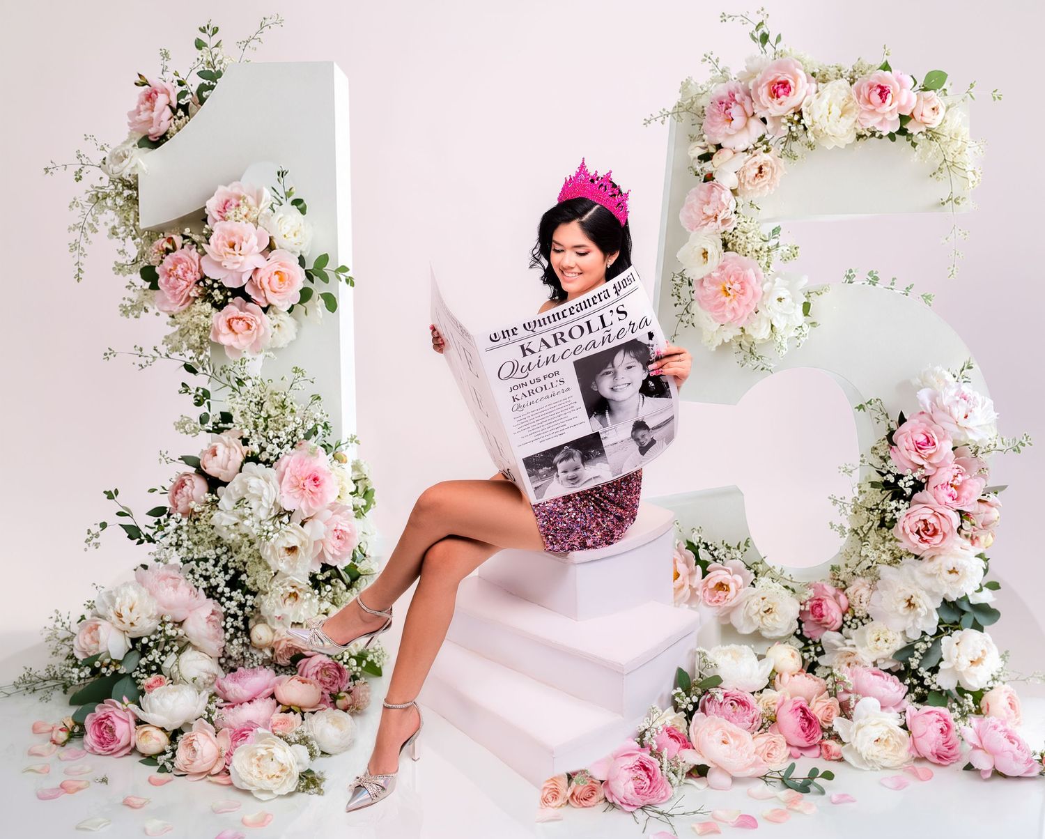 Young woman in pink floral dress sits among large floral number 15 decorations for a quinceañera celebration.
