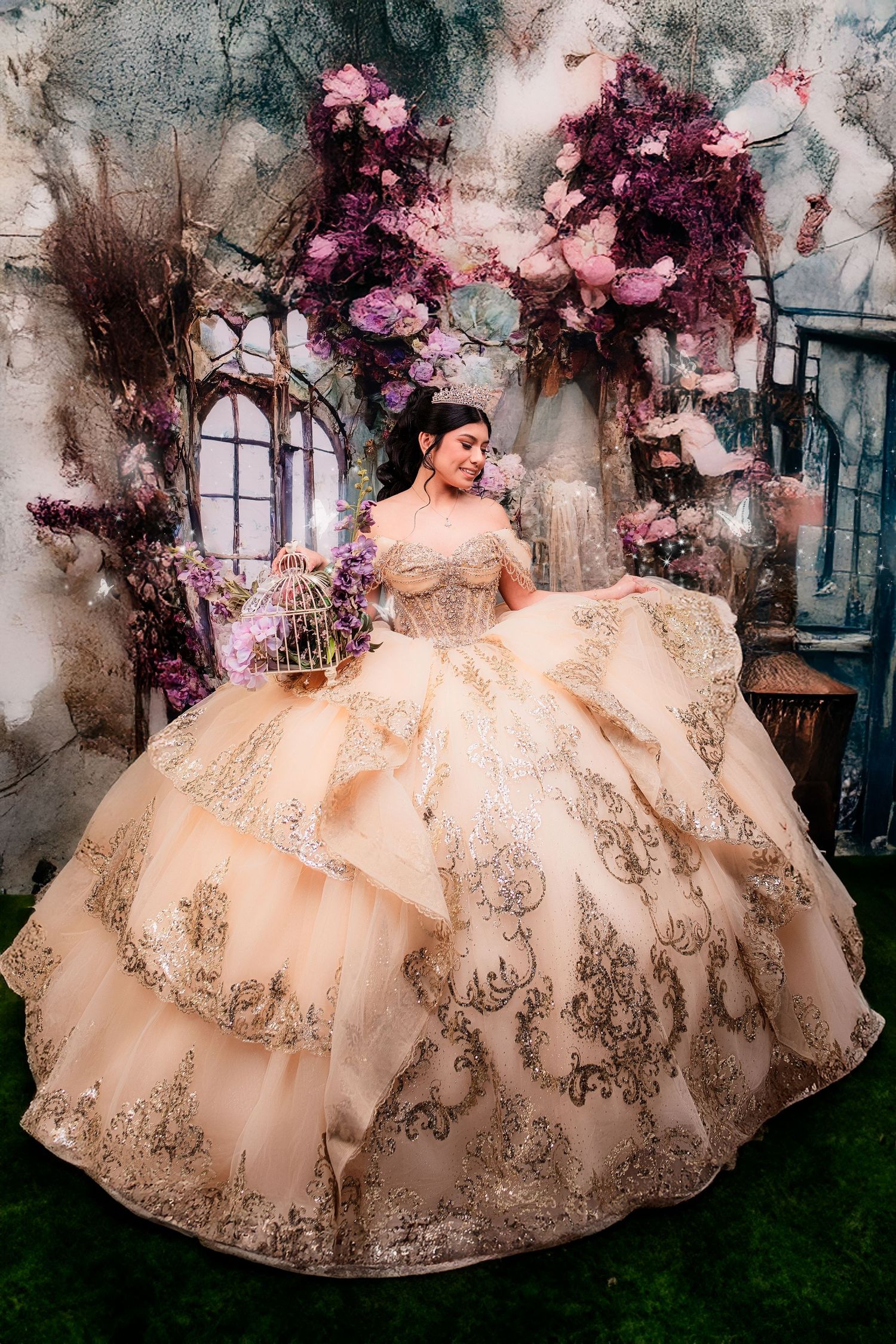 A woman in a stunning gold quinceañera ball gown with intricate lace details poses among purple floral decorations.