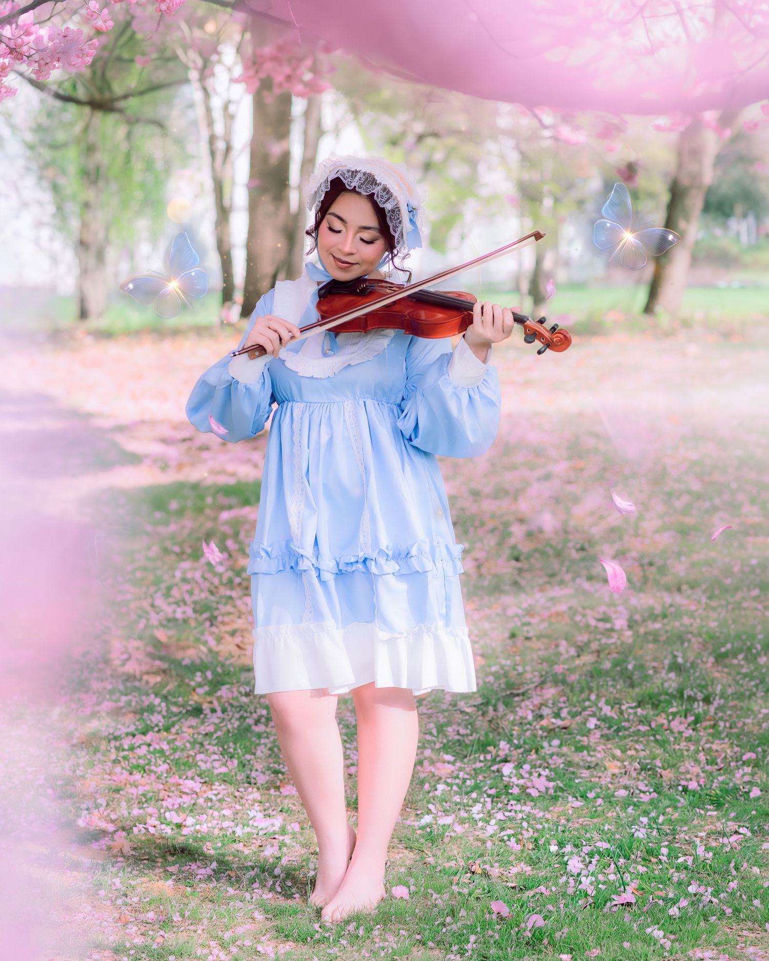 Sweet 16 photo session featuring a young woman in a light blue dress and bonnet plays violin outdoors among blooming cherry blossom trees.