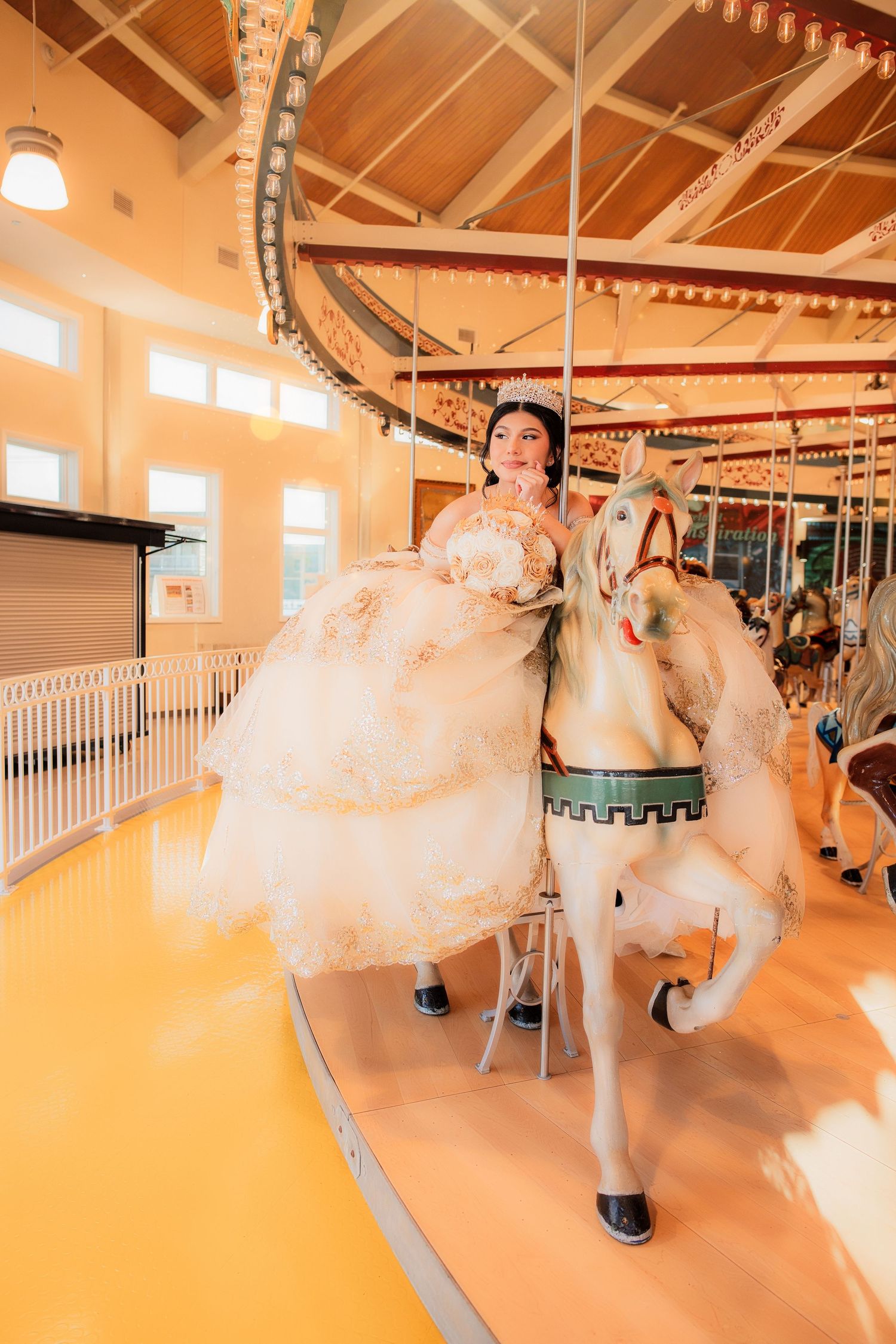 A bride in a white ball gown poses on a carousel horse inside a classic merry-go-round pavilion.