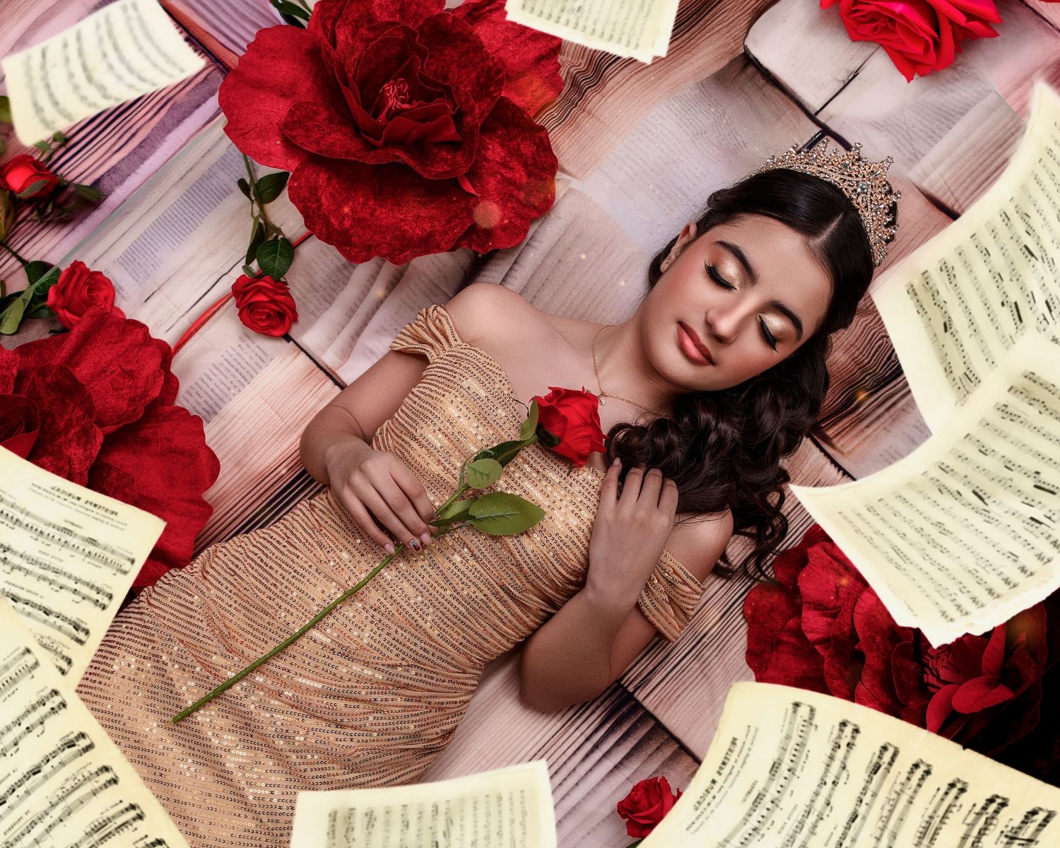 Young woman in gold dress holds red rose surrounded by sheet music and roses in artistic portrait. Beauty and the Beast inspired photo shoot