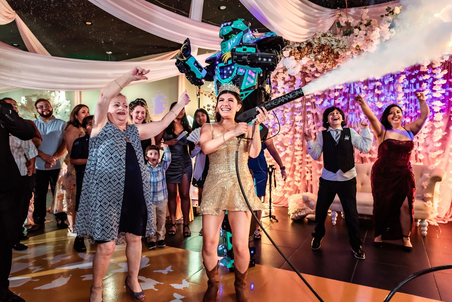 Lively wedding reception with guests dancing and celebrating, woman in gold dress holding microphone on dance floor.