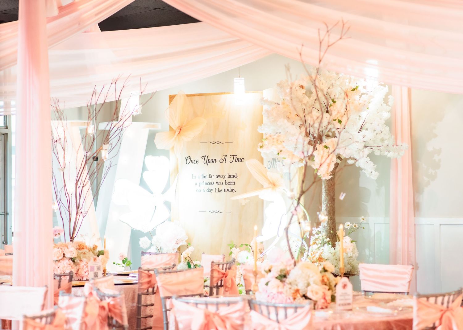 Elegant wedding reception with pink draping, white floral centerpieces, and a romantic fairy-tale themed backdrop.