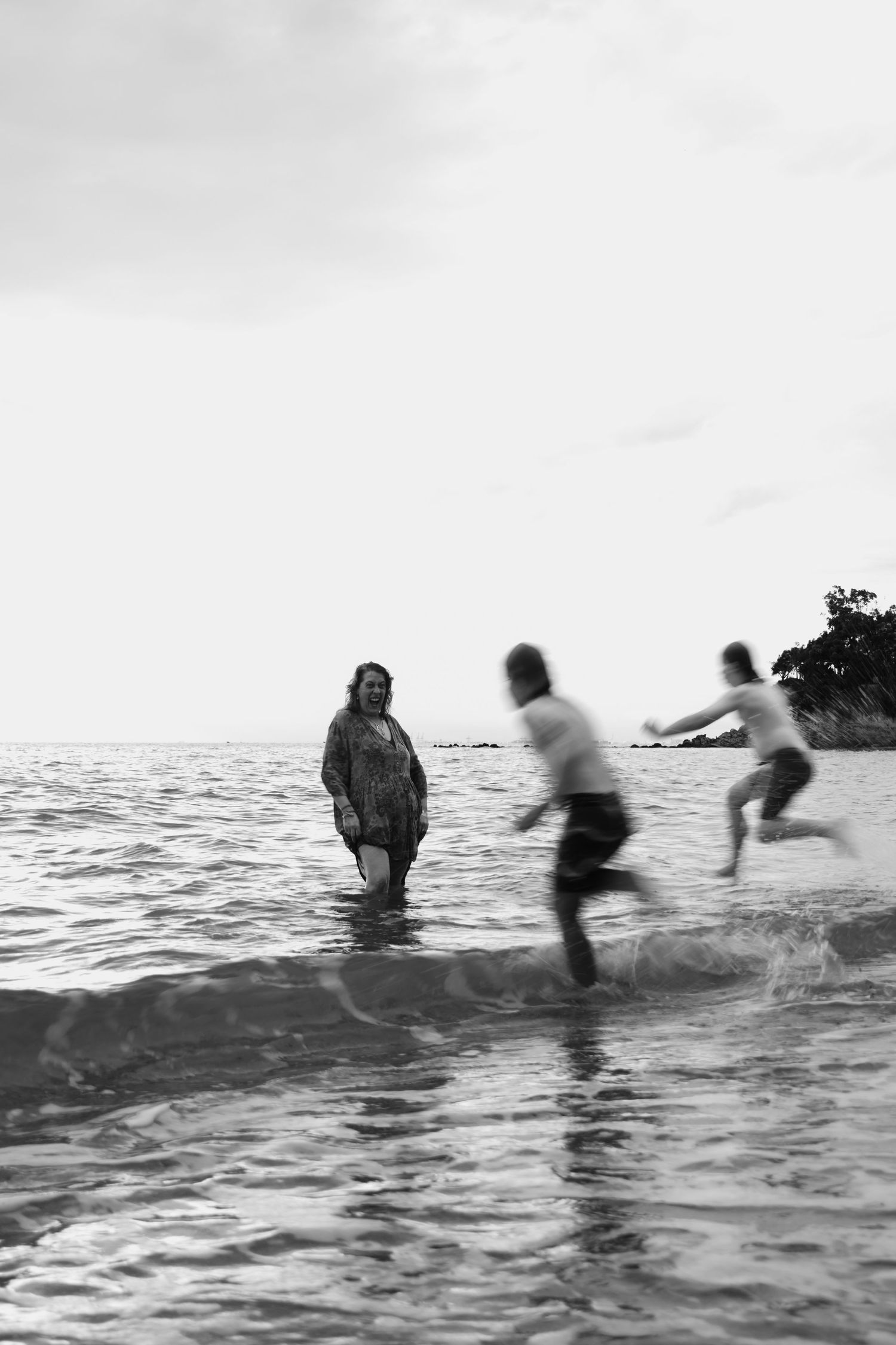 woman in the water at the beach watching her children run into the water